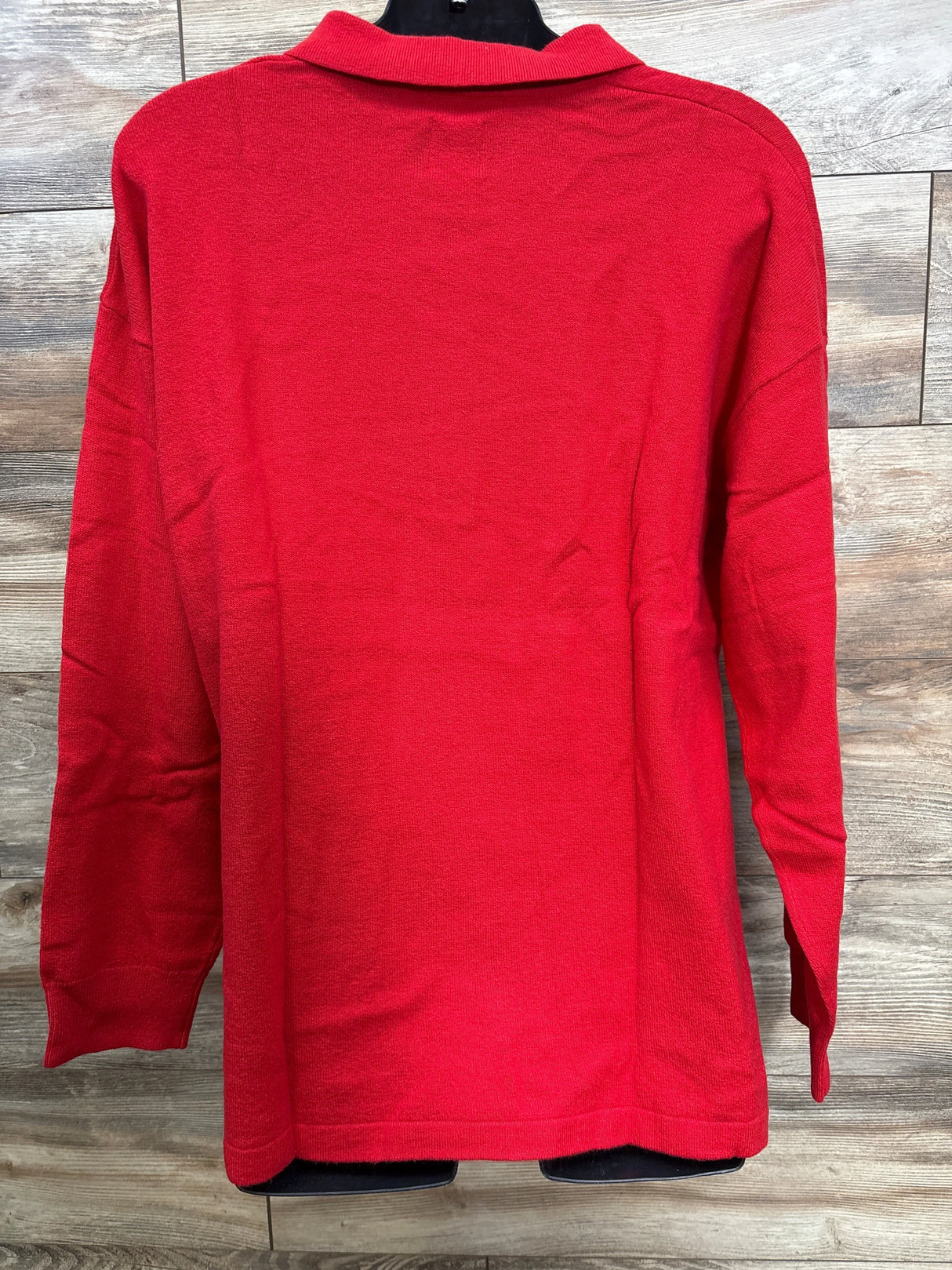 Back view of vibrant red long-sleeve sweater on black hanger against wood background