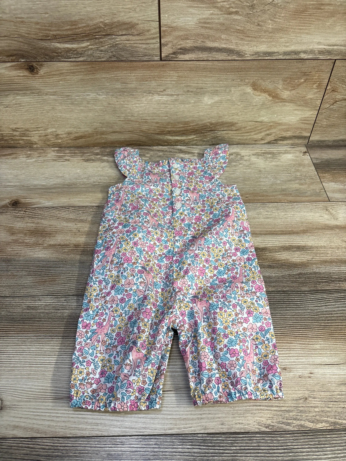 Flat lay of smocked floral sleeveless baby jumpsuit size 6-12m showcasing ruffle shoulder straps and elasticized leg hems on wood background