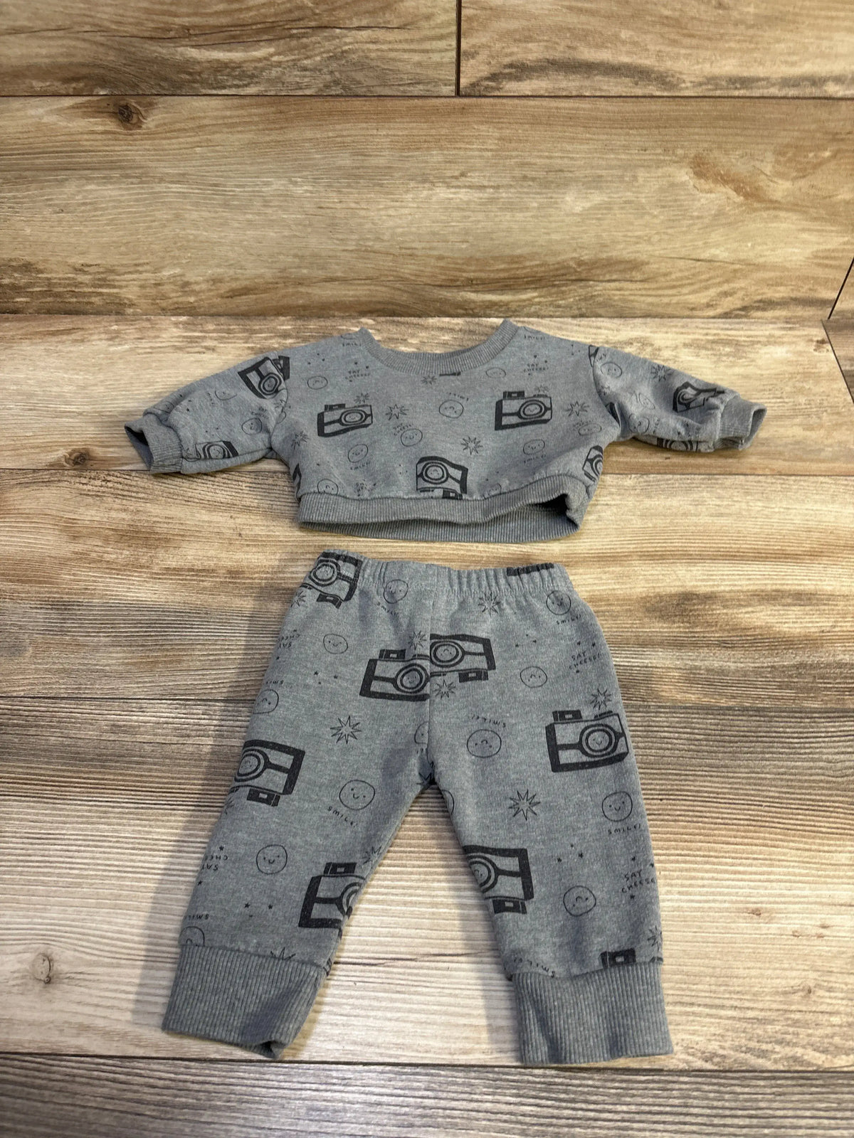 Top view of Cat & Jack 2pc Say Cheese sweatshirt and joggers set with camera prints and ribbed cuffs on wood-look flooring