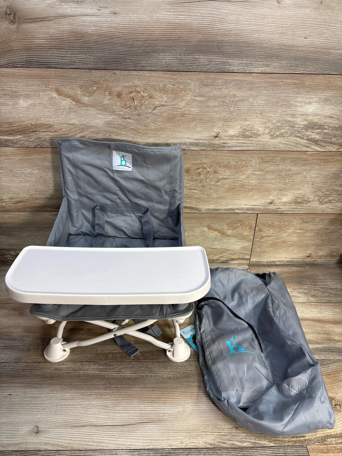 Front view of gray Hiccapop OmniBoost folding booster chair showcasing the tray and carry bag on a wood floor