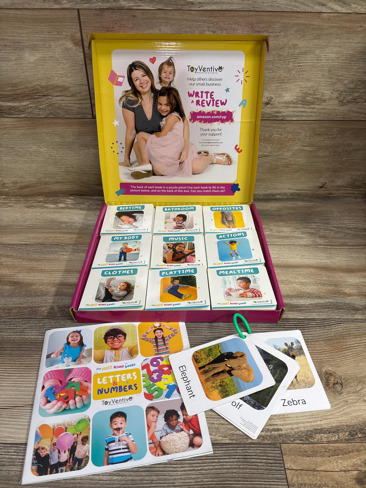 Open box of Toyventive My First Board Books for Girls 18ct set with themed books and animal flashcards on a wood floor