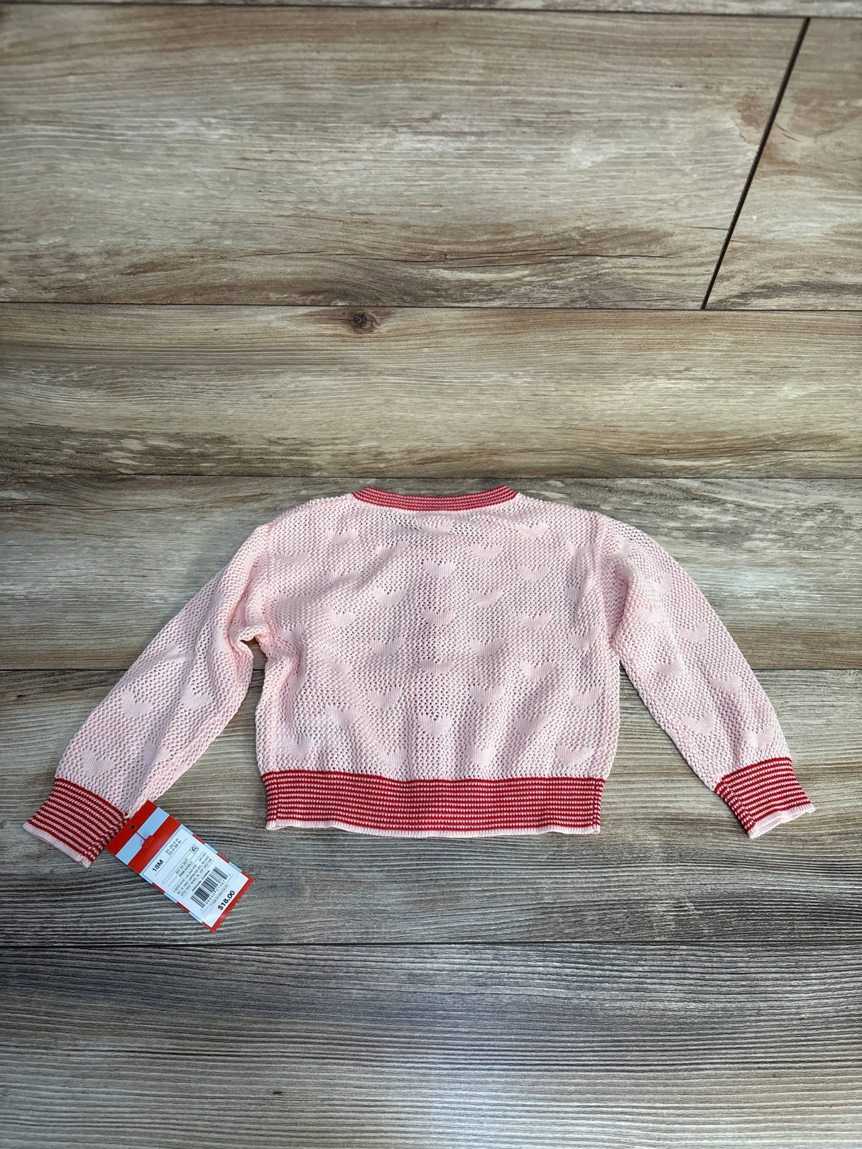Pink knit toddler sweater with heart pattern and red striped cuffs on wood background