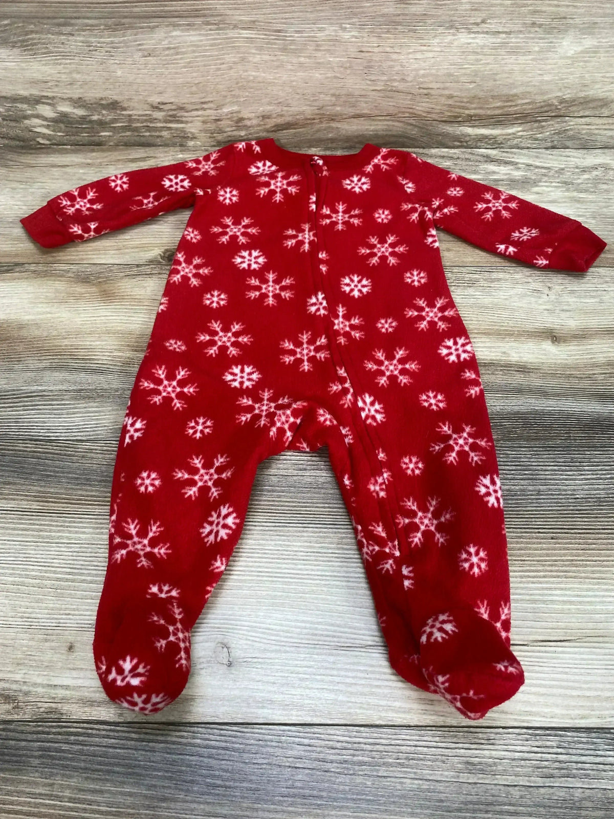 Top-down view of red snowflake footed baby sleeper with front zipper on light wood background