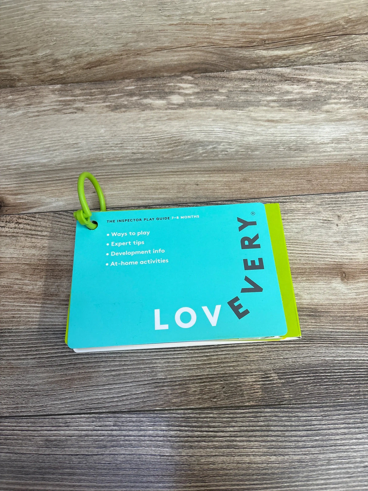 Lovevery play guide booklet for 7-8 months on wood table, green binder ring