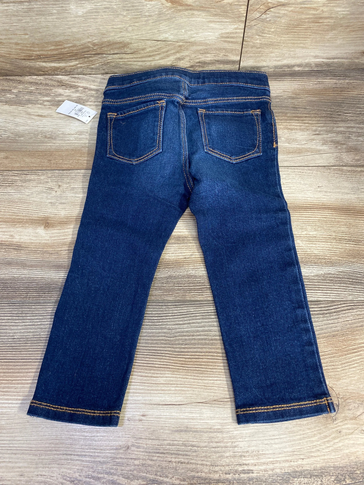 Dark blue toddler jeans with back pockets and tan stitching on wooden floor