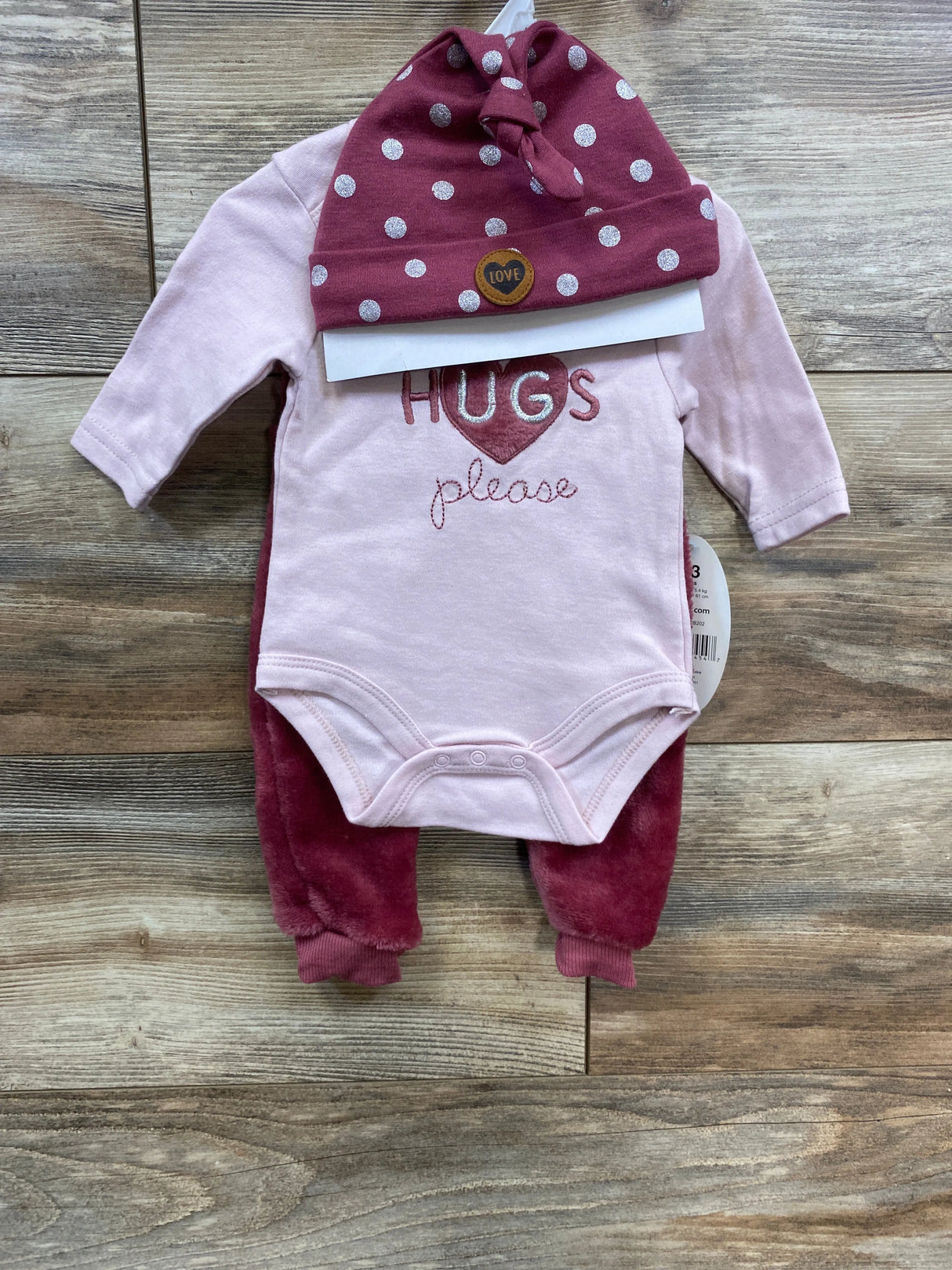 Pink baby outfit set with polka dot hat and 'HUGS please' bodysuit on wood floor