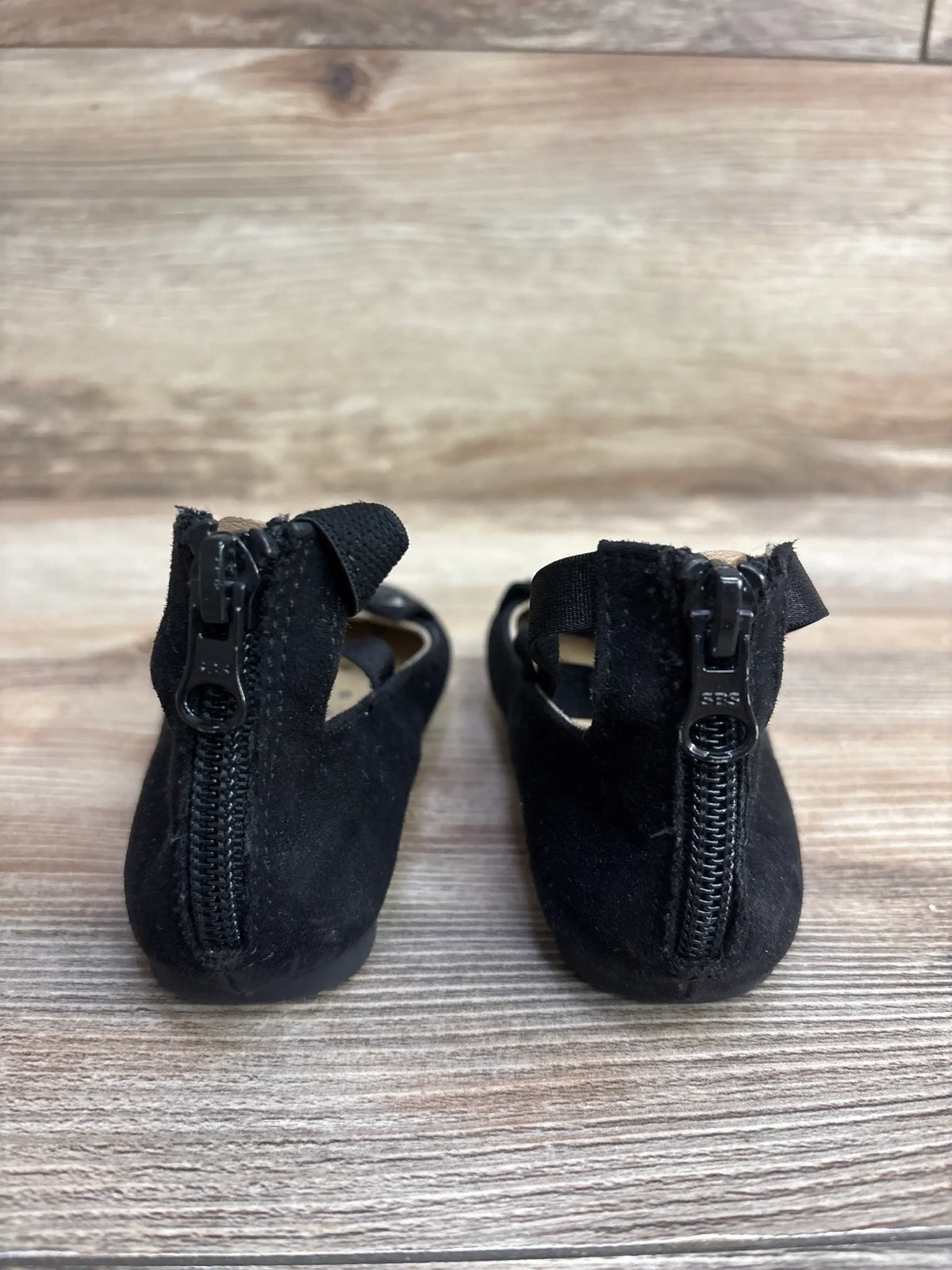 Back view of Cat & Jack Trinity ankle strap ballet flats in black showcasing rear zipper closures and suede texture on wood floor