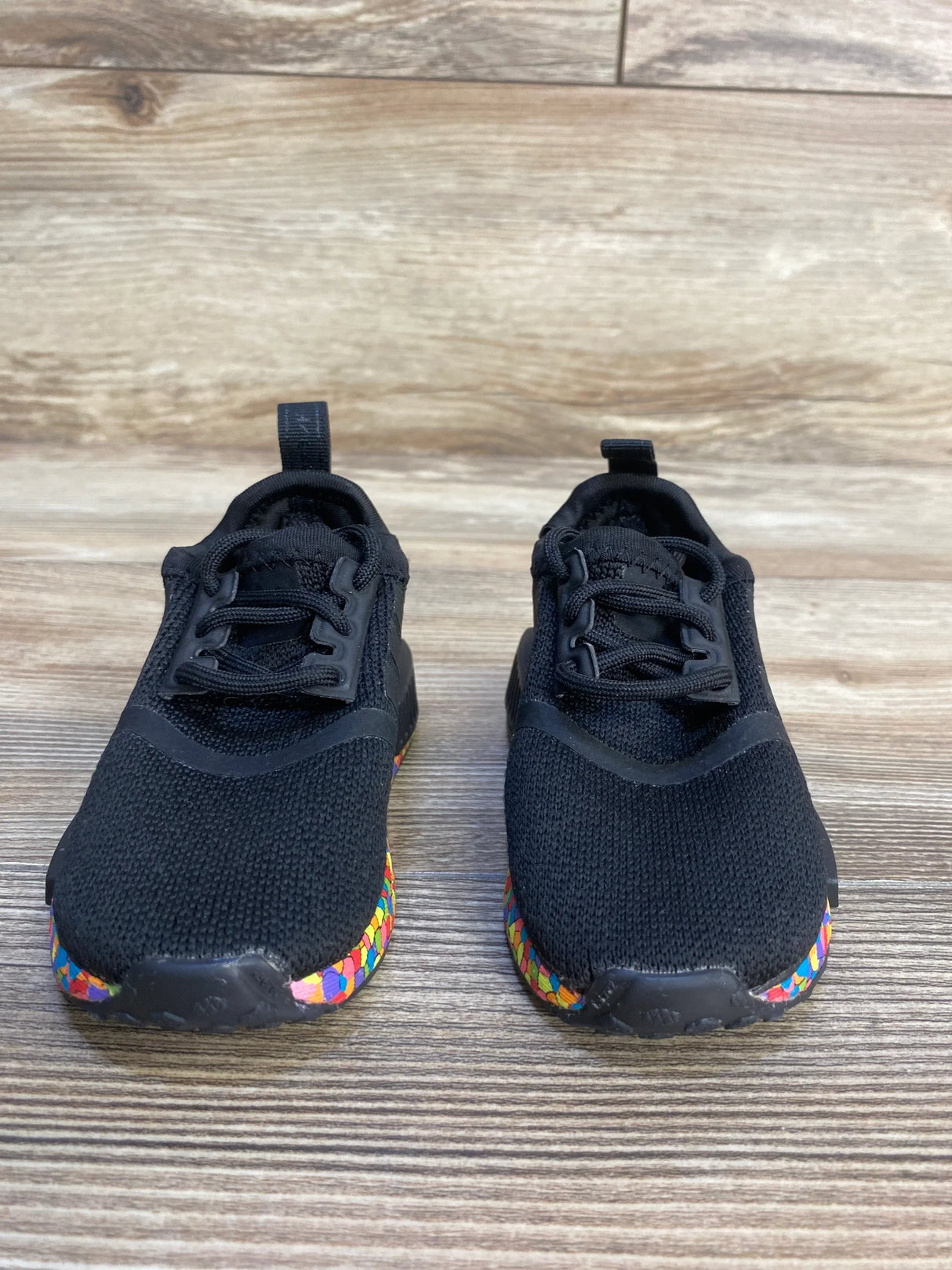 Black kids athletic shoes with colorful soles on wood background