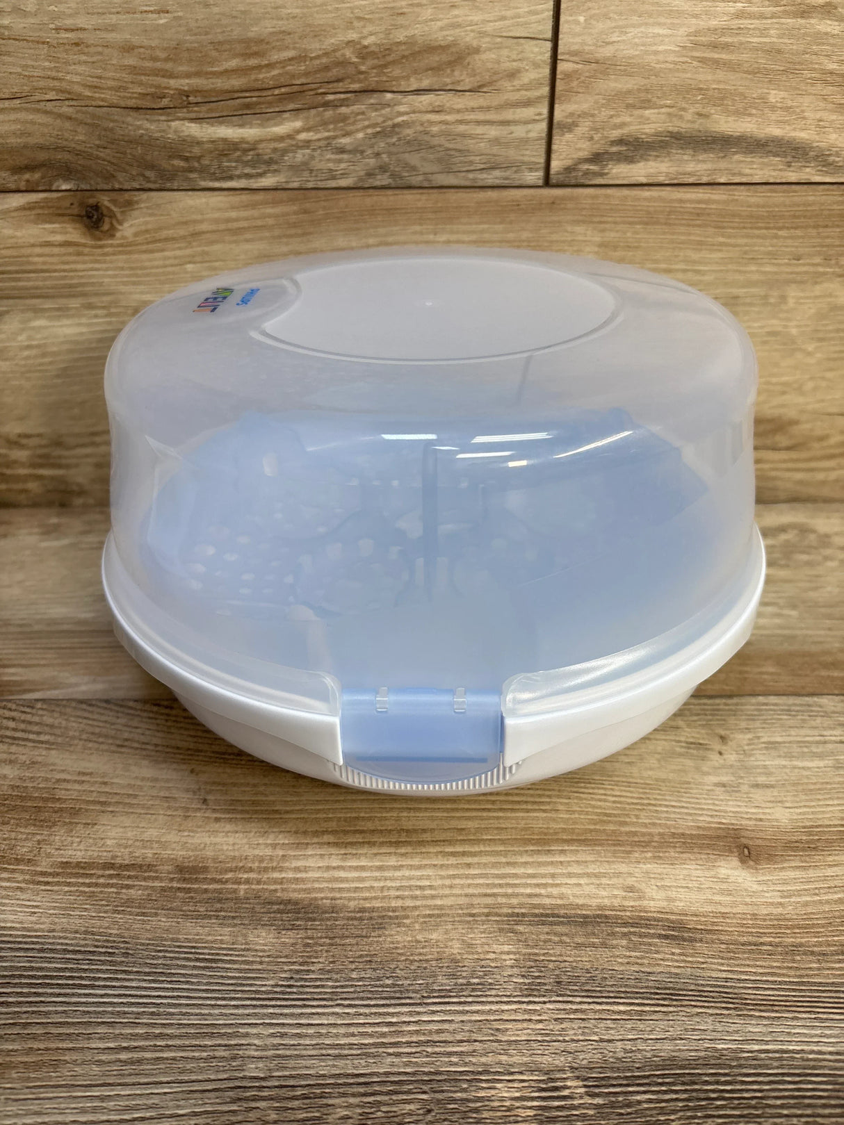 Front view of AVENT microwave steam sterilizer showcasing translucent frosted lid and blue front latch on wooden surface