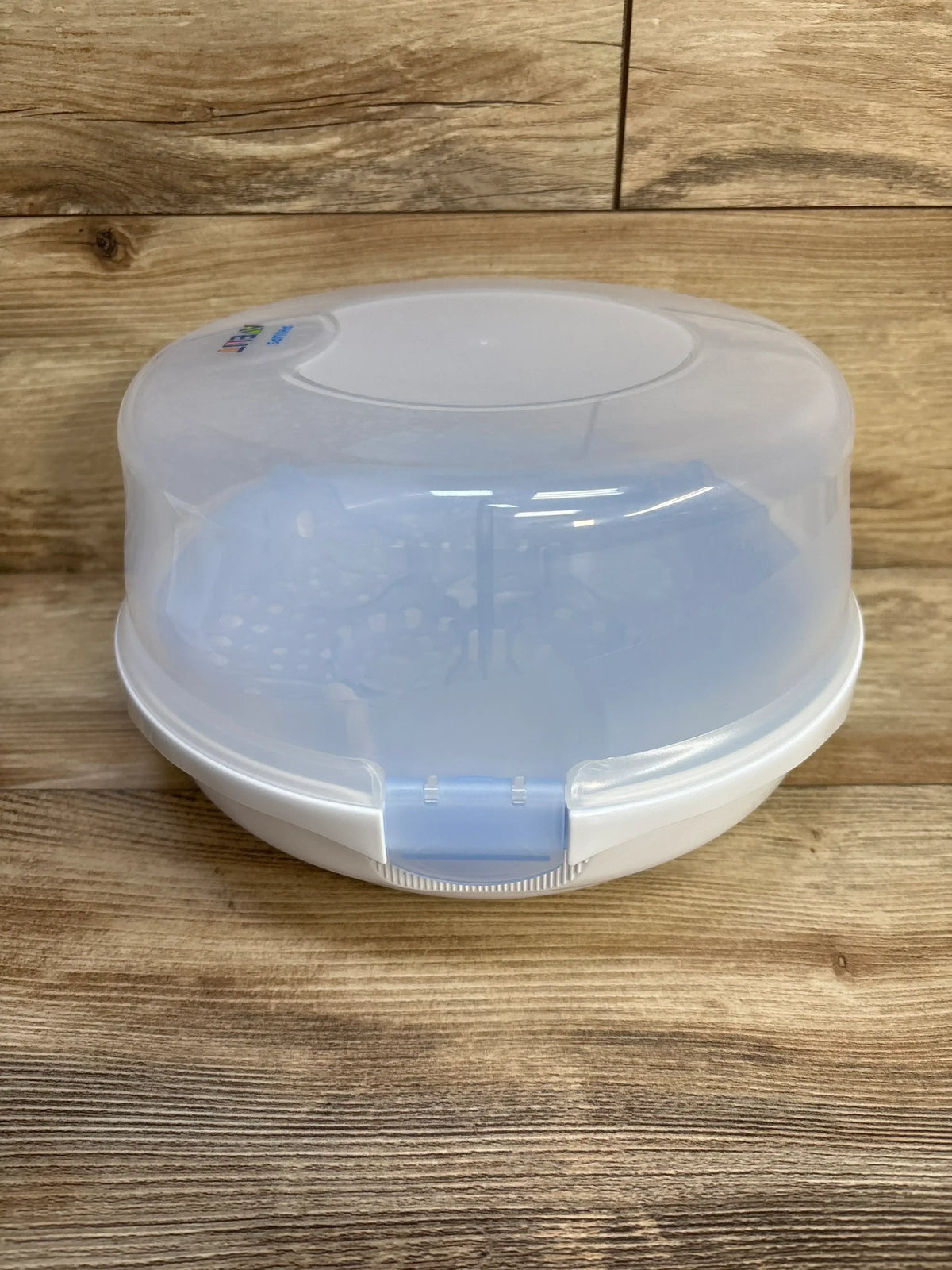 Front view of AVENT microwave steam sterilizer showcasing translucent frosted lid and blue front latch on wooden surface