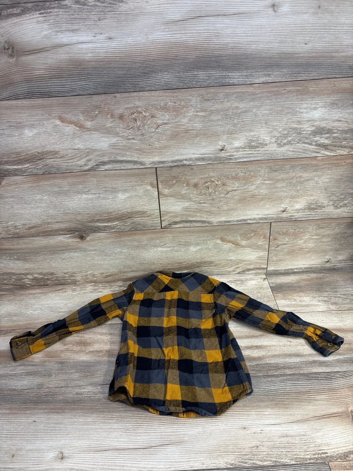 Children's long-sleeve plaid flannel shirt in yellow and black laid flat on wood floor