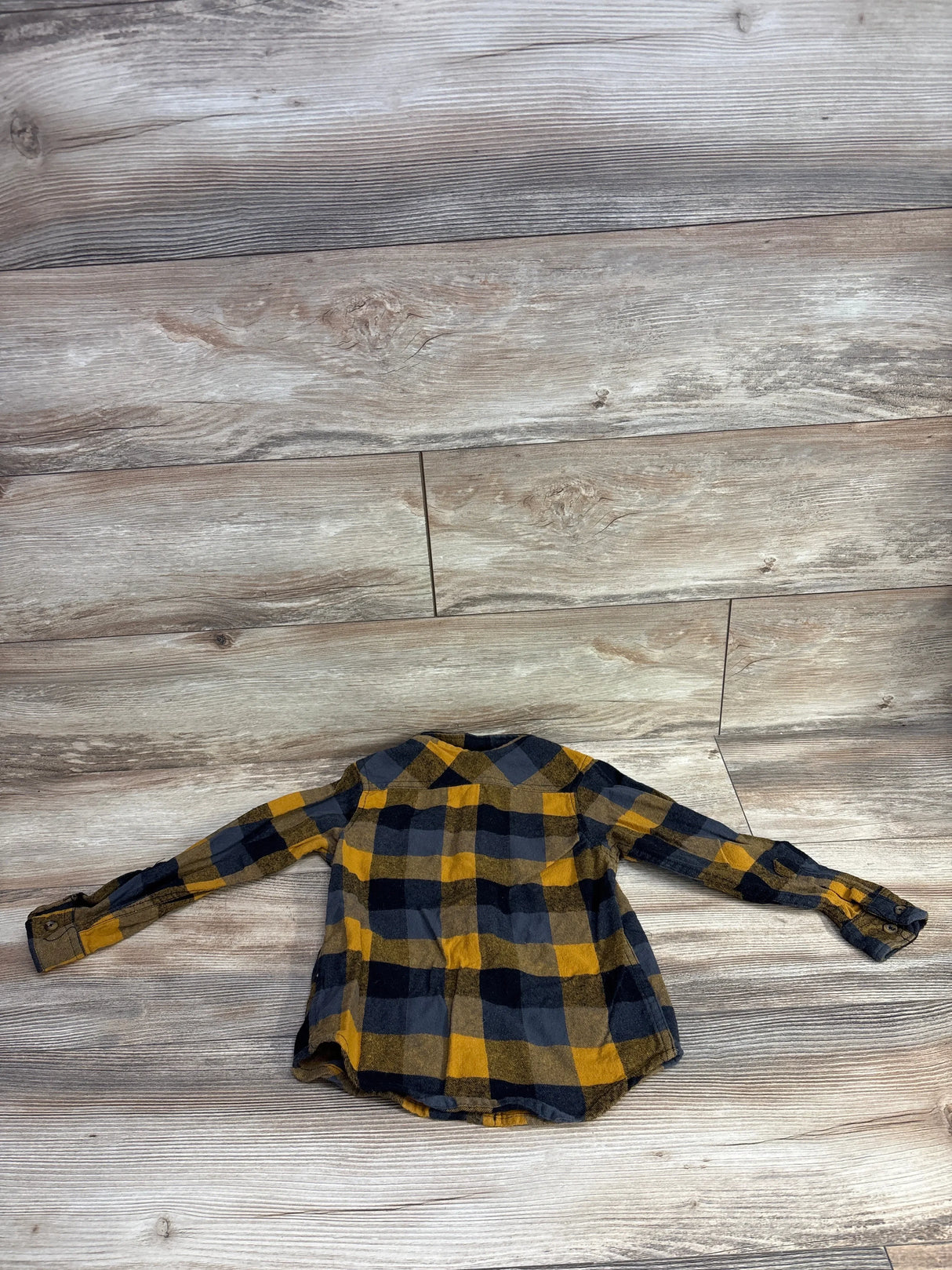 Children's long-sleeve plaid flannel shirt in yellow and black laid flat on wood floor