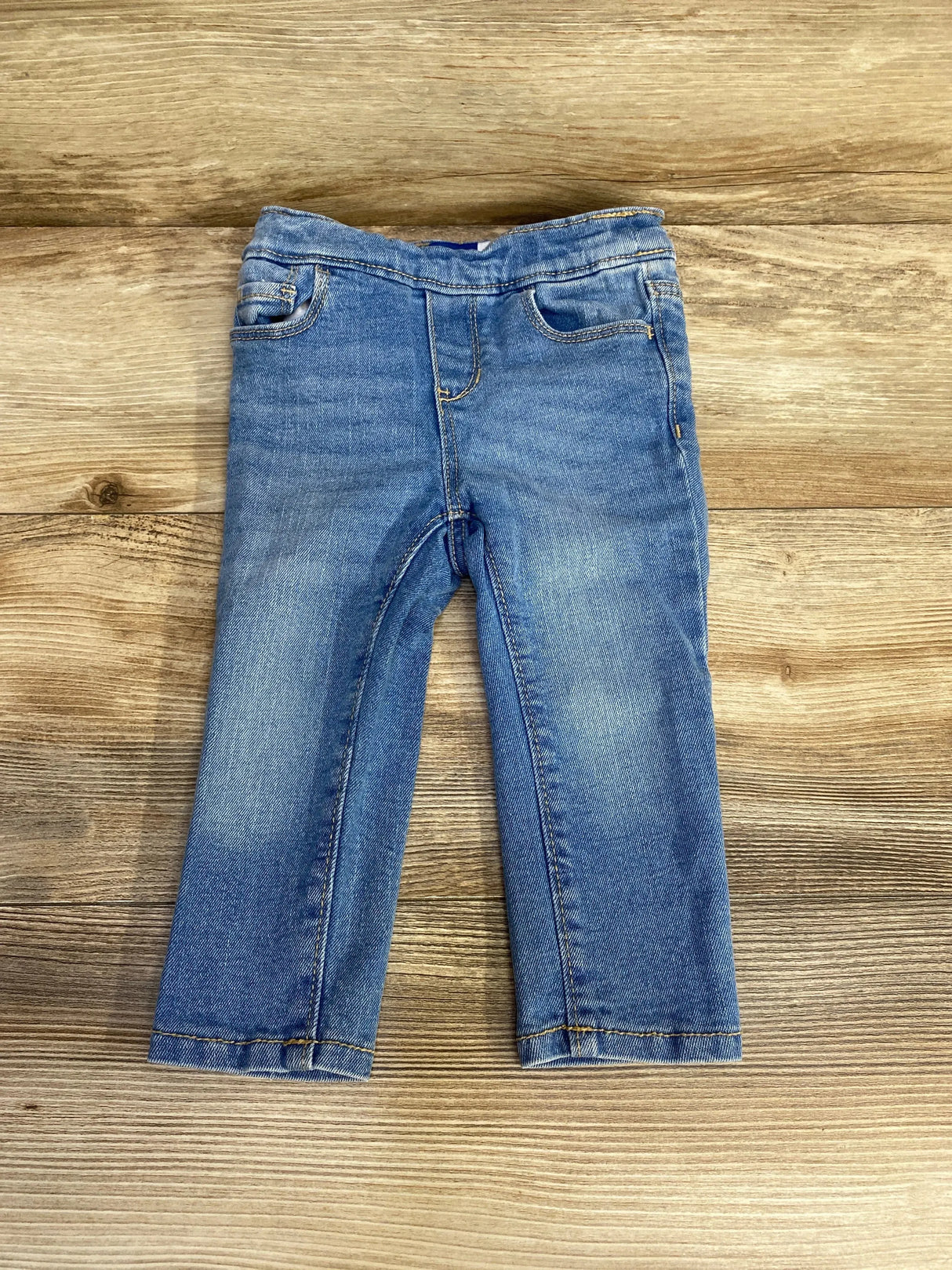 Front flat lay of Old Navy toddler skinny jeans showcasing faded wash and elasticized waistband on wood background