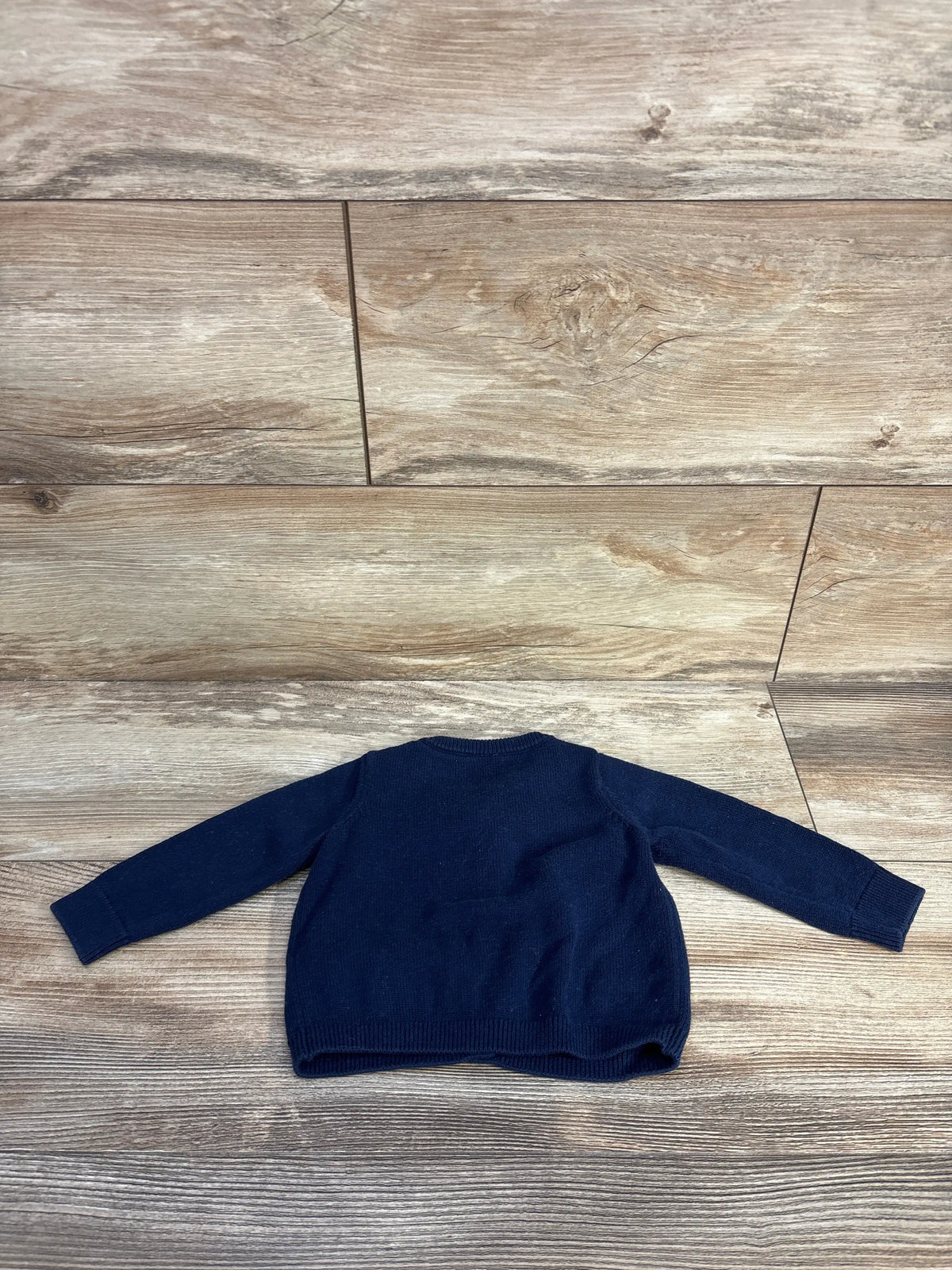 Flat lay of Edgehill Collection navy knit cardigan for 3-month babies, showcasing long sleeves on a wood-grain floor
