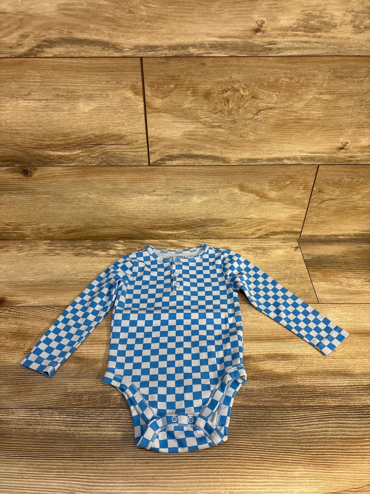 Front view of Old Navy blue checkered Henley bodysuit, size 18 to 24 months, with long sleeves and snap closures on wood floor