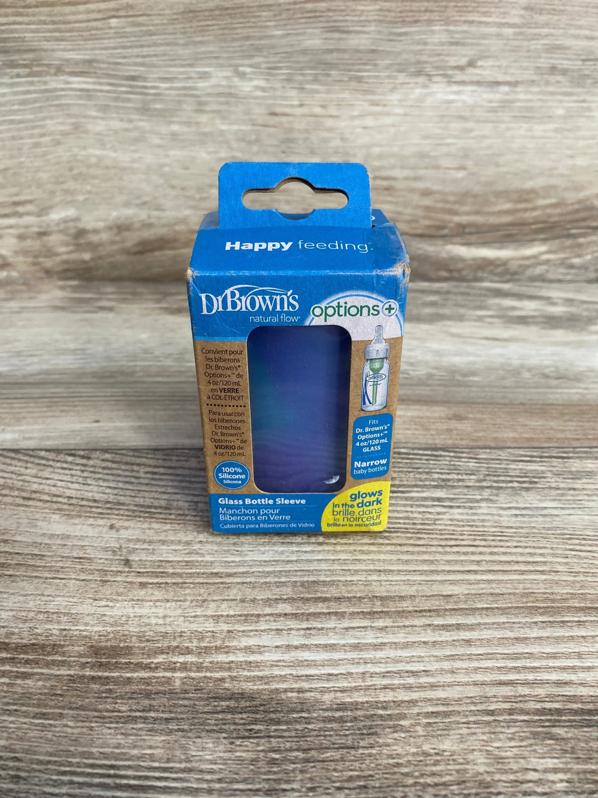 Front view of Dr. Brown’s Options Plus glass baby bottle sleeve 4 oz glow in the dark in original blue retail box on wood plank floor