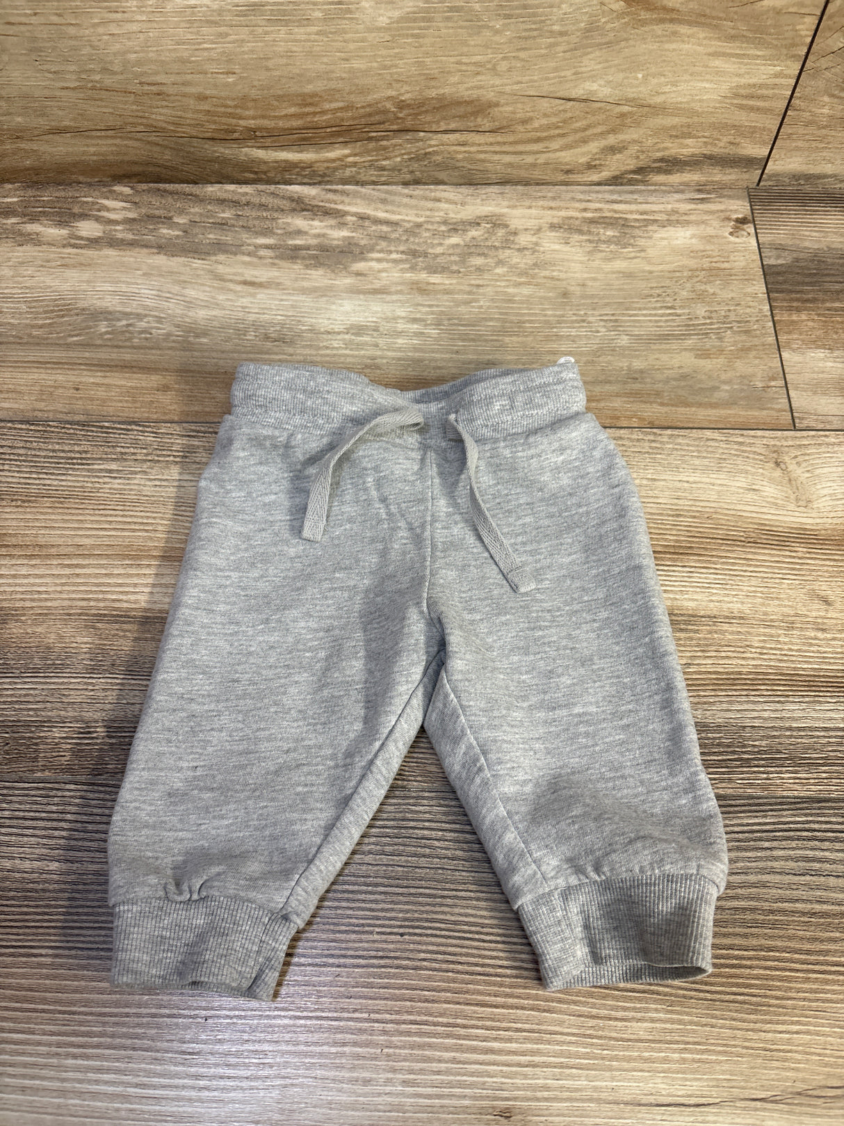 Front view of H&M grey drawstring joggers, size 3 months, with adjustable waist and ribbed cuffs on wood flooring