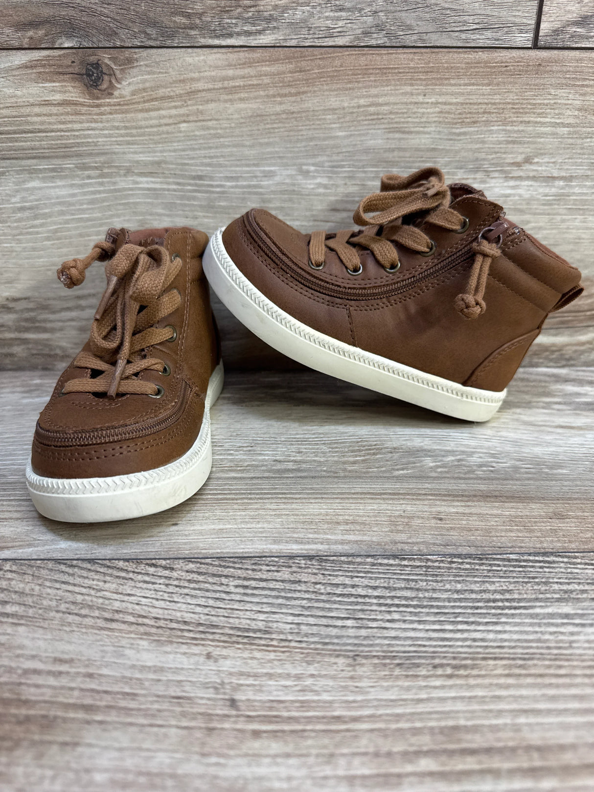 Three-quarter view of Harmon brown high-top sneakers showing lace-up front, side zipper and white sole on wood background