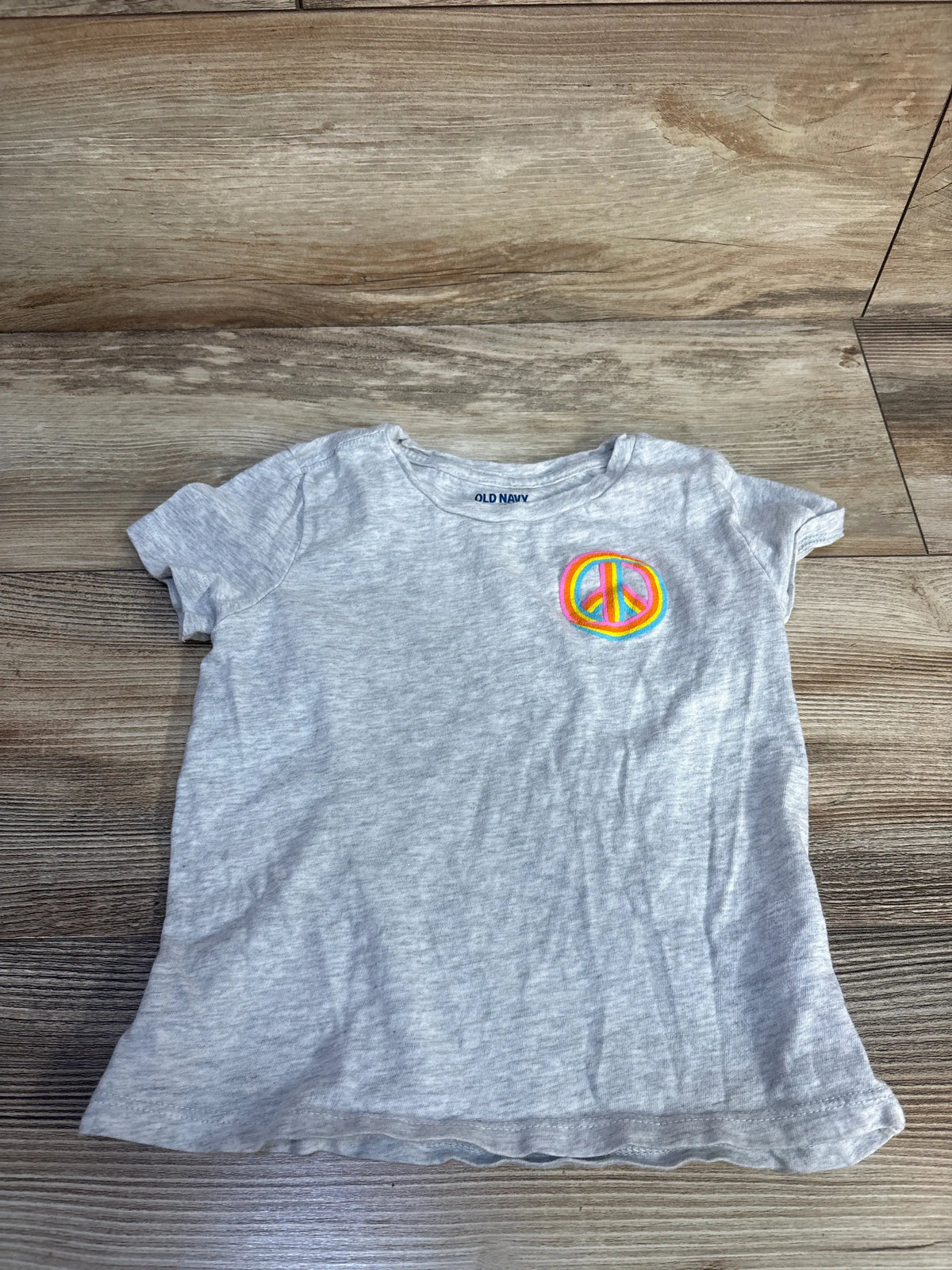 Front view of a grey Old Navy children’s shirt showcasing a colorful peace sign graphic on a wood floor