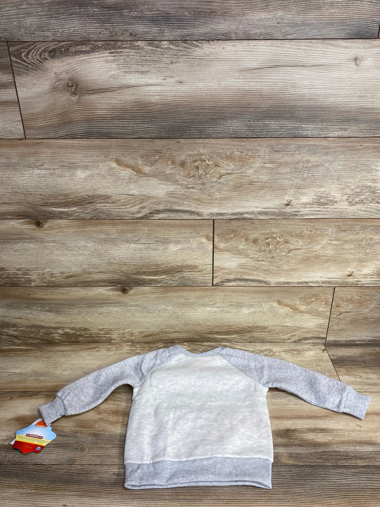 Light gray and white long sleeve baby sweatshirt with tag on wooden background