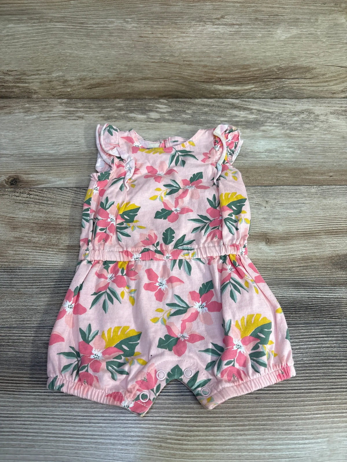 Front flat lay of pink floral baby romper size 3m showing ruffle sleeves, elastic waist and snap crotch on wood background