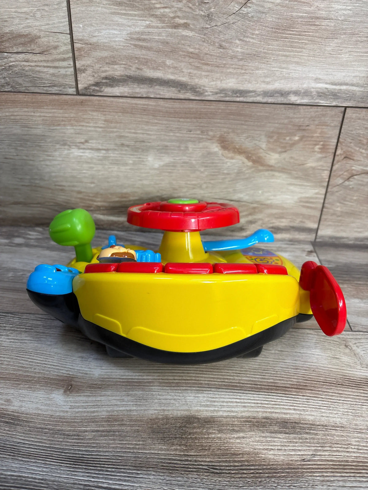 Side view of Vtech Turn & Learn Driver showcasing colorful steering wheel, buttons, and signal lever with a wood look background