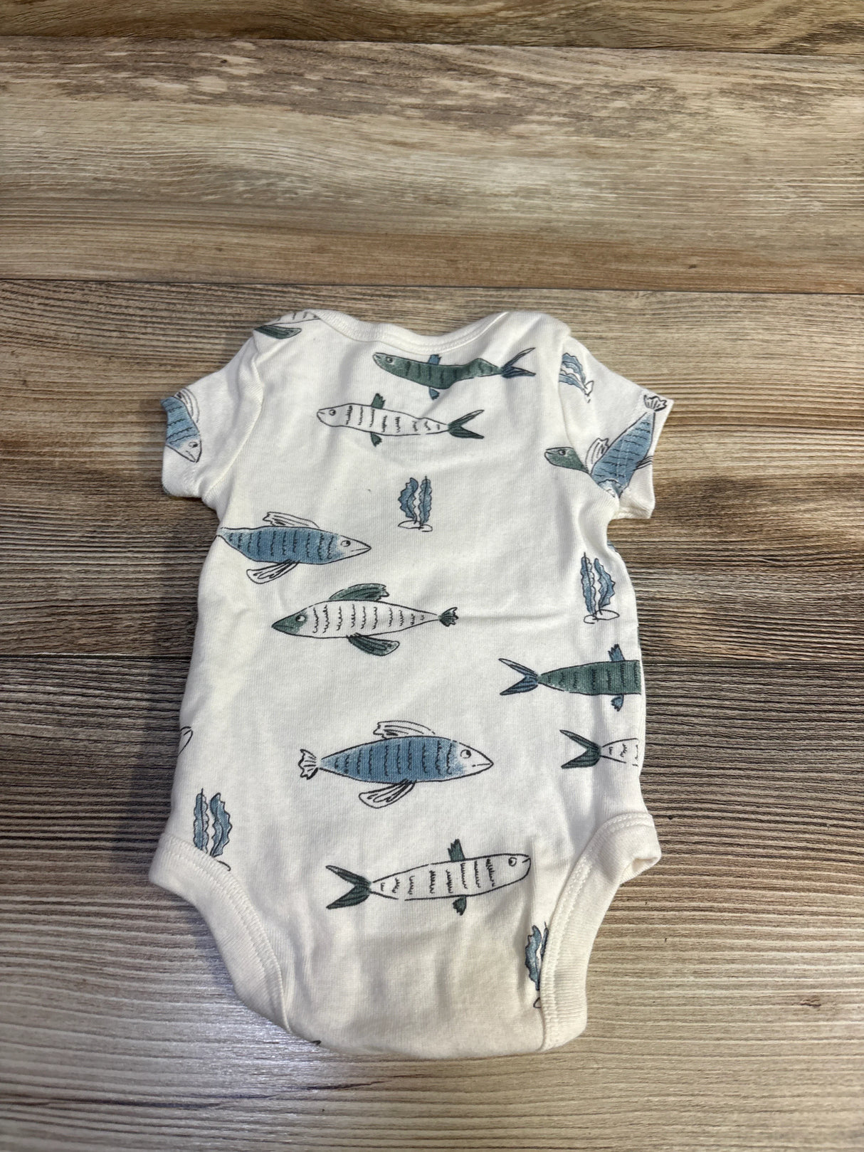 Back view of Little Planet organic newborn bodysuit showcasing blue and green fish print and snap crotch on wood background