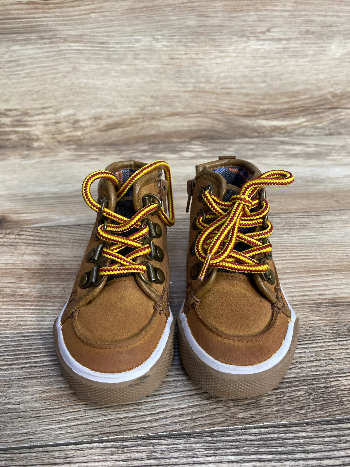 Brown children's hiking shoes with yellow and red laces on wooden background