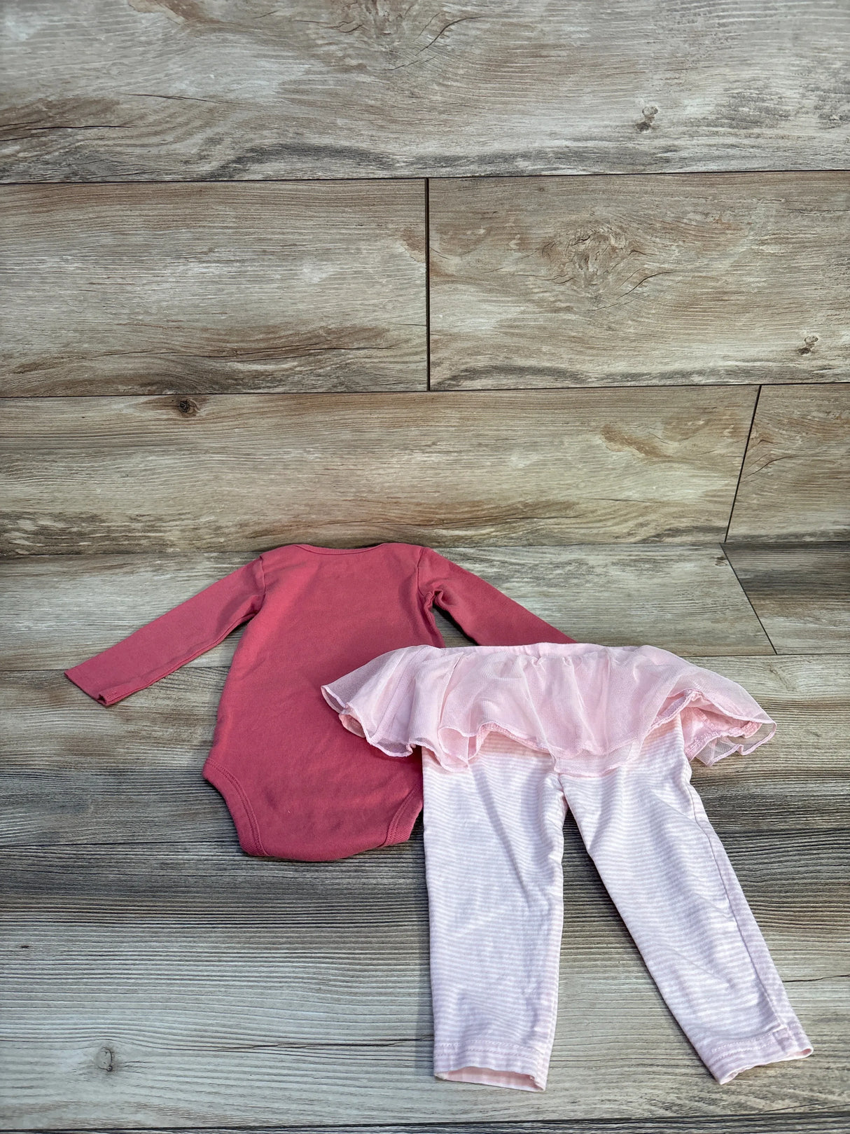 Long sleeve pink baby bodysuit and pink striped leggings with tulle skirt on wood floor