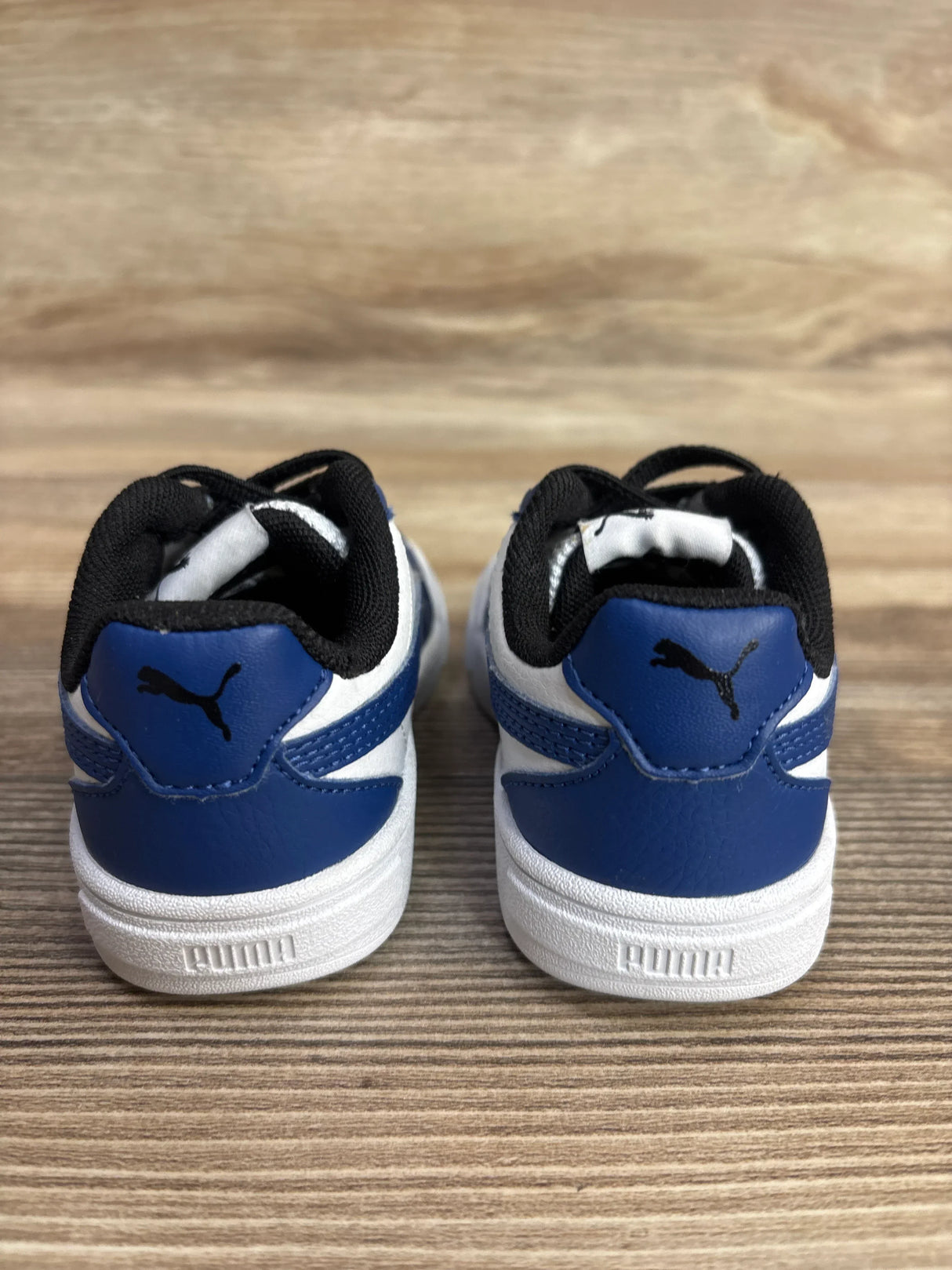 Blue and white toddler sneakers with black logo on wooden background