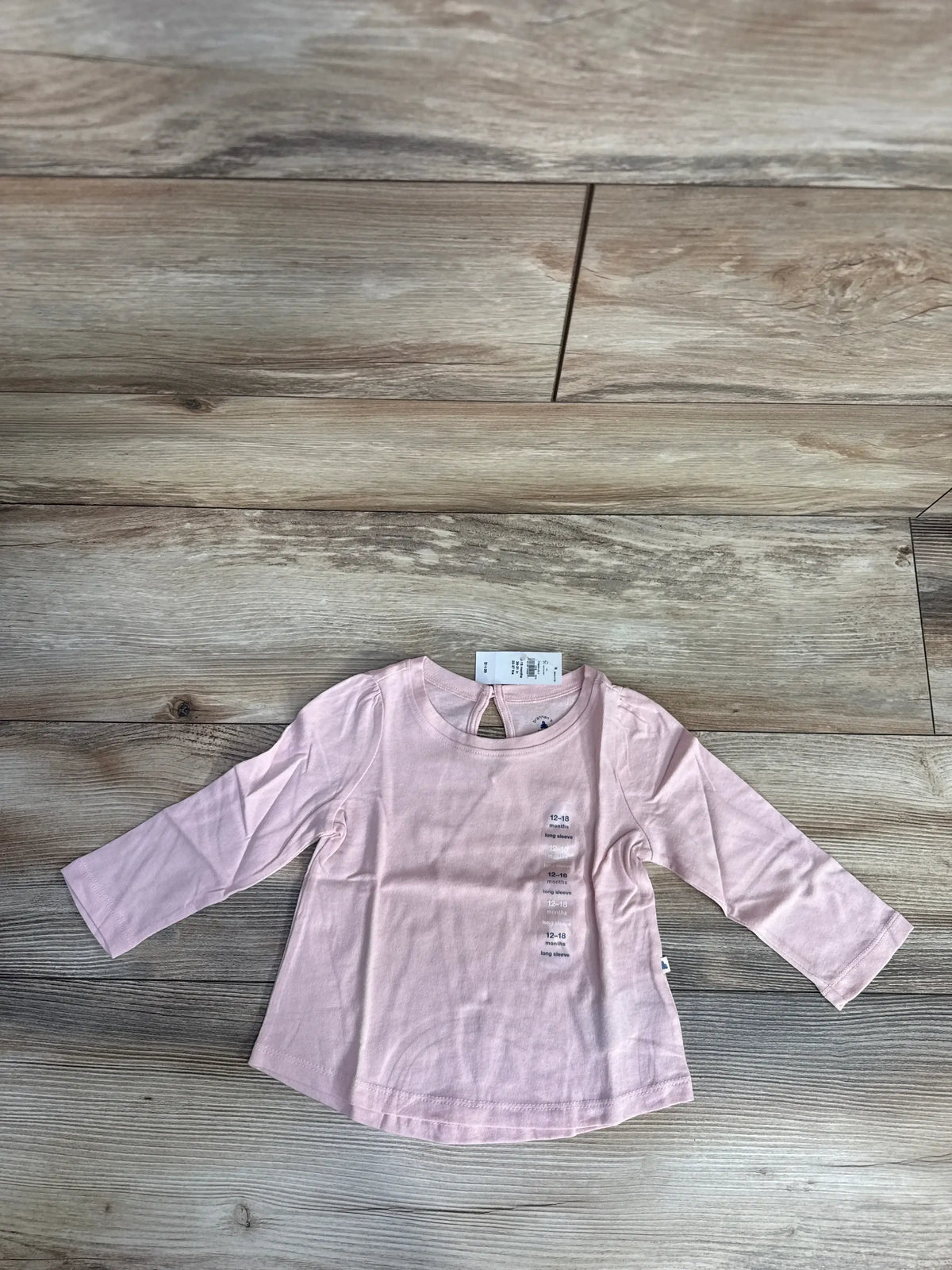 Light pink long sleeve baby shirt with tags on wooden floor