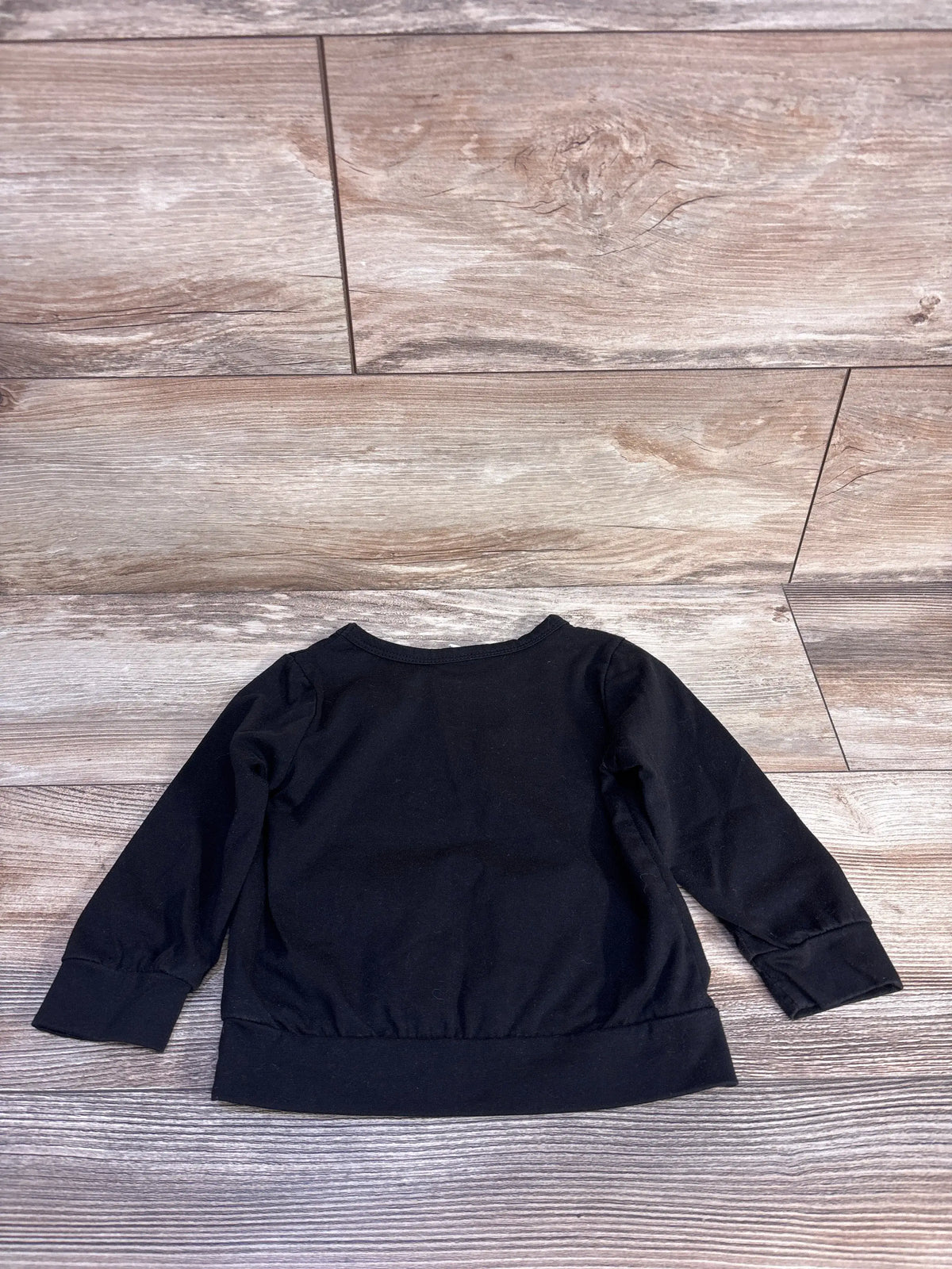 Top view of Shein Daddy’s Little Dude shirt showcasing black long sleeves and ribbed cuffs on a wood-look floor