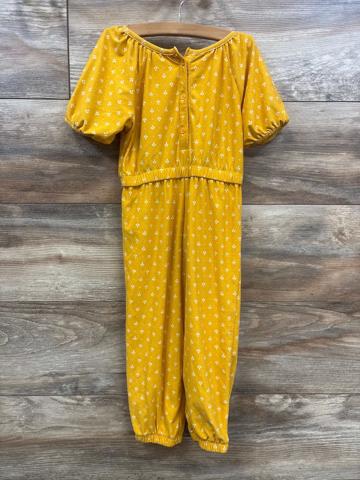 Front view of Old Navy jumpsuit showcasing mustard yellow with white diamond print puff sleeves and elastic cuffs on hanger against wood