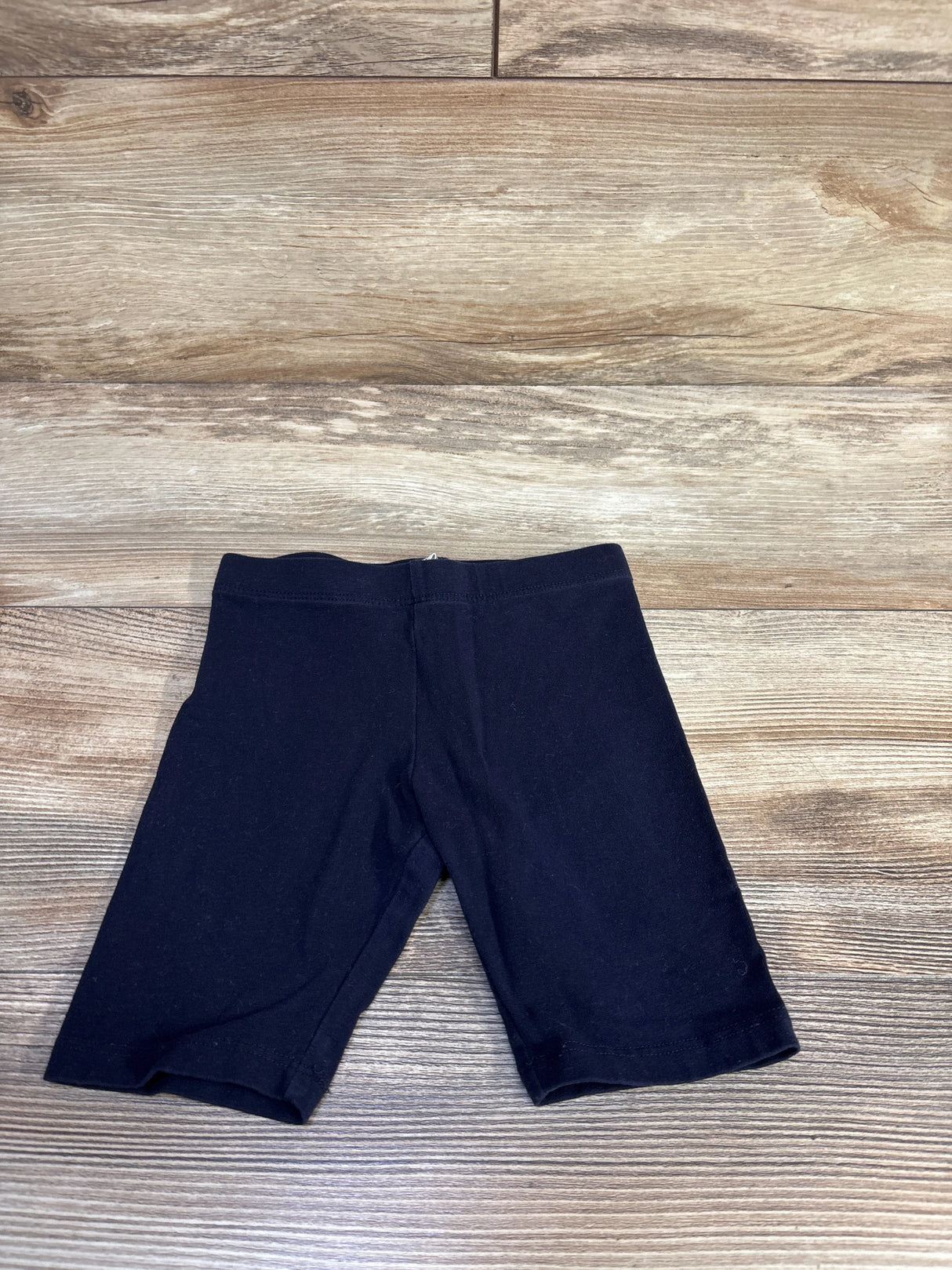Flat lay of H&M navy toddler bike shorts size 4T showing elastic waistband and mid-thigh length on wood background
