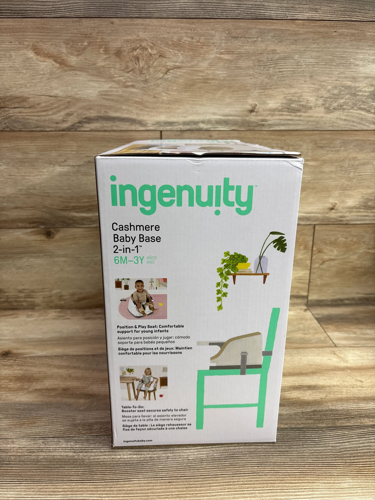 Front view of Ingenuity Cashmere Baby Base 2-in-1 seat box showing booster and floor seat uses on a wood floor