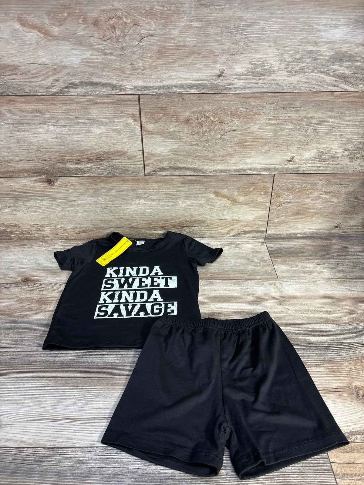 Front view of black Shein toddler shirt and shorts set with Kinda Sweet Kinda Savage graphic on wood-look background