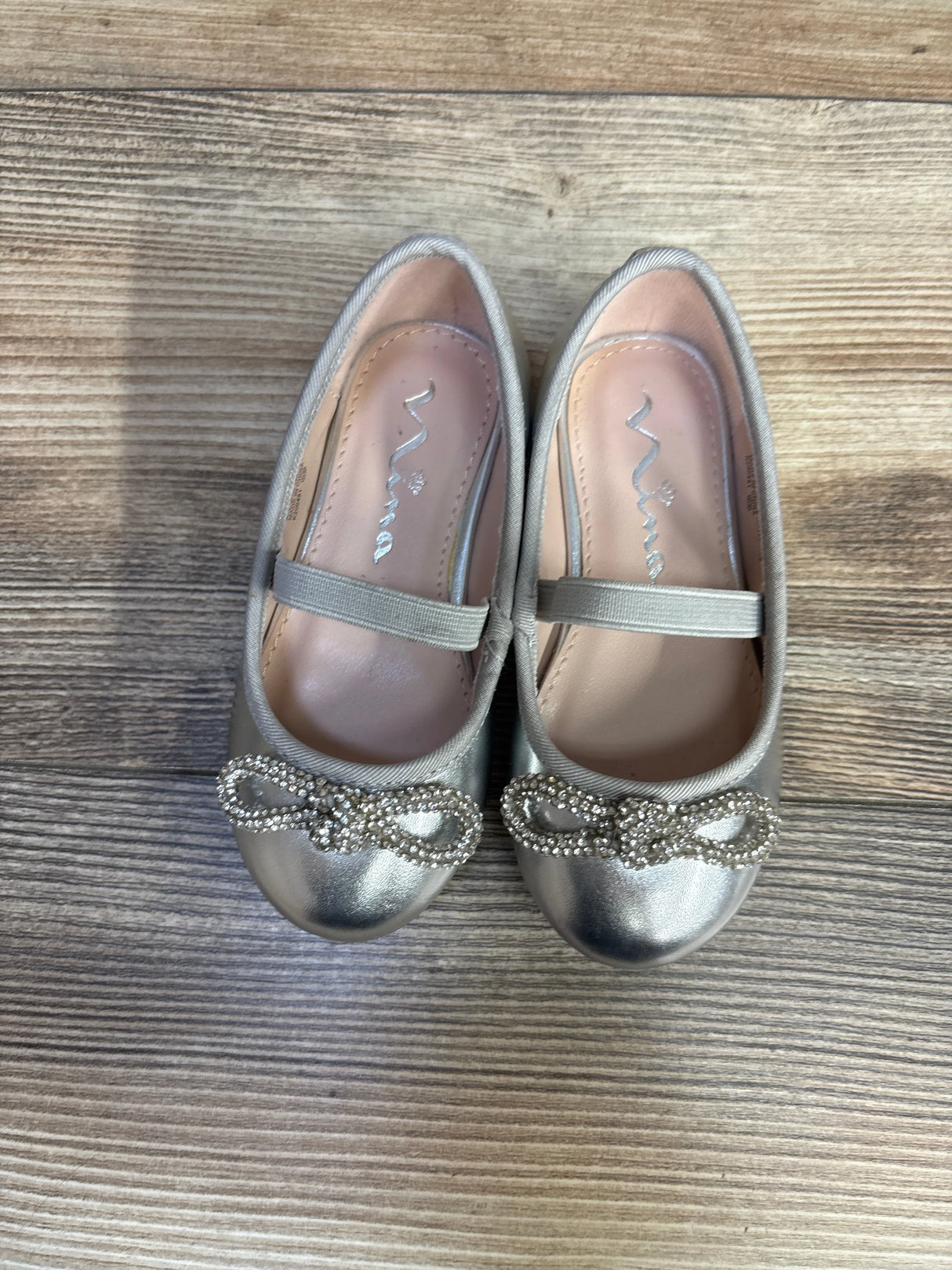 Silver girls' dress shoes with rhinestone bow detail on wooden floor