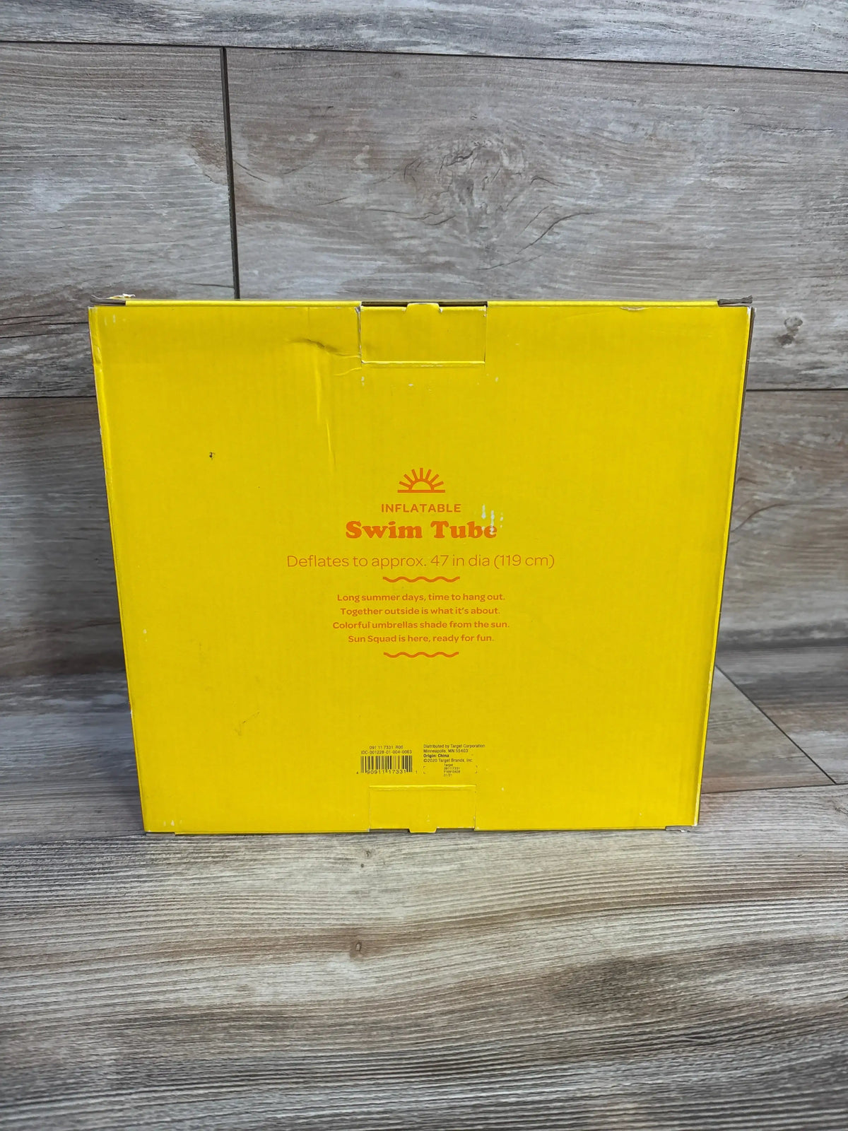 Front of boxed Sun Squad inflatable swim tube showing 'Swim Tube' headline and printed 'deflates to approx. 47 in (119 cm)' text on wood floor