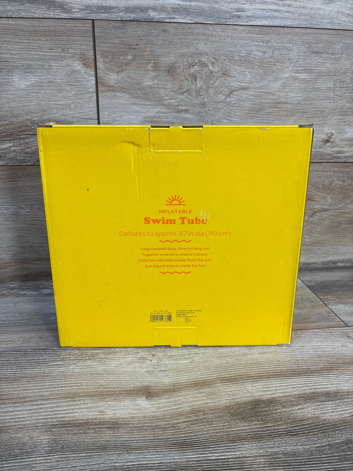 Front of boxed Sun Squad inflatable swim tube showing 'Swim Tube' headline and printed 'deflates to approx. 47 in (119 cm)' text on wood floor