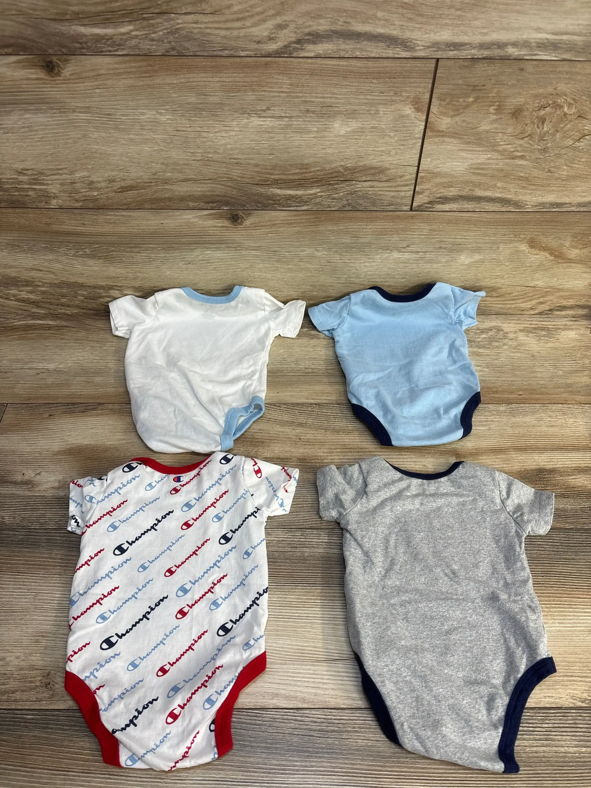 Top-down view of Champion 4-pack bodysuit set (3M) with one logo-print and three solid colors on wood floor