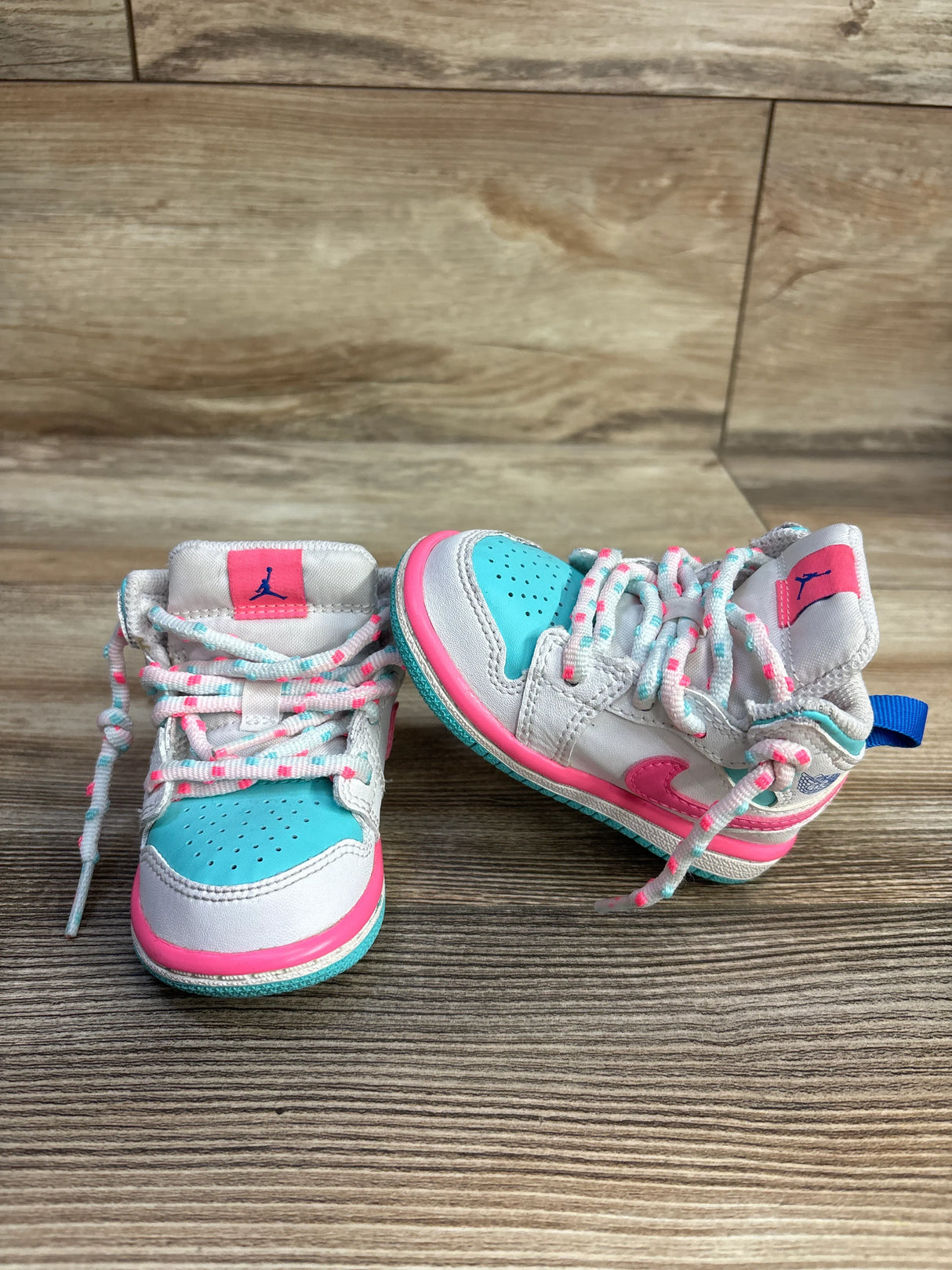 Colorful toddler Air Jordan sneakers with teal, pink, and white on a wood floor