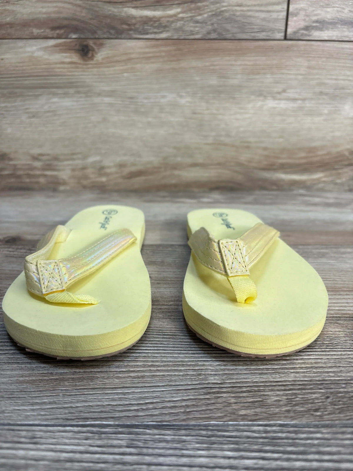 Yellow children’s flip flops with foam soles on wood background, kids summer footwear