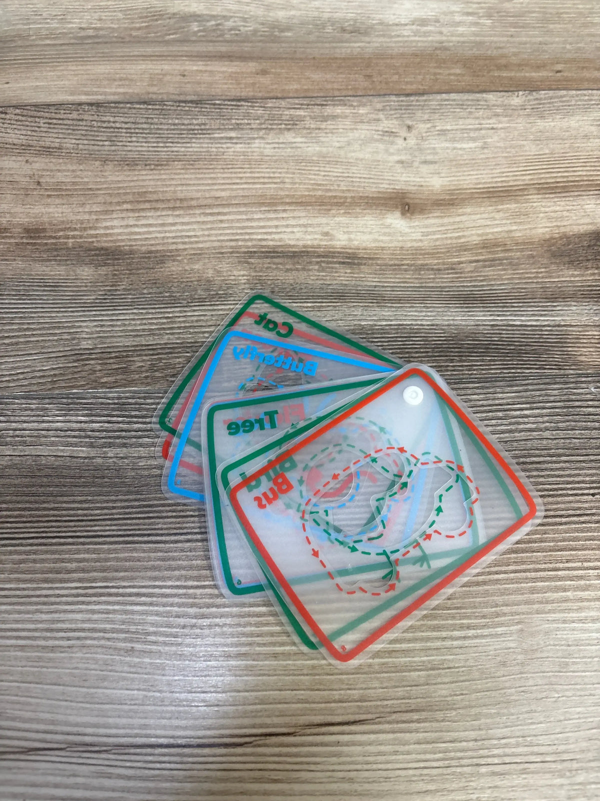 Angled view of eight laminated tracing cards fanned to show colored borders and dashed tracing lines on a wood tabletop