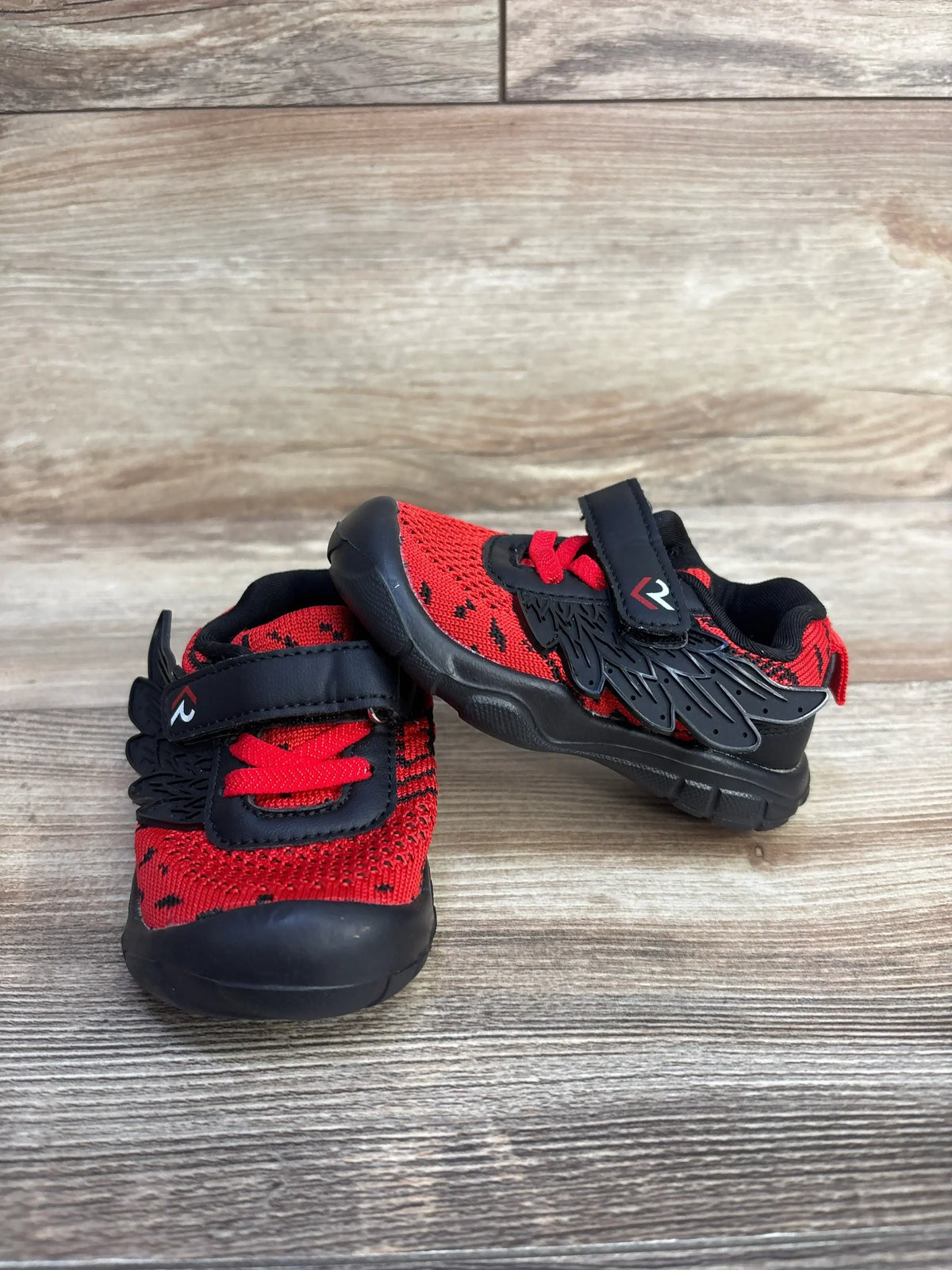 Three-quarter view of boy’s red and black wing sneakers size 3.5C showing wing detail and Velcro strap on white background