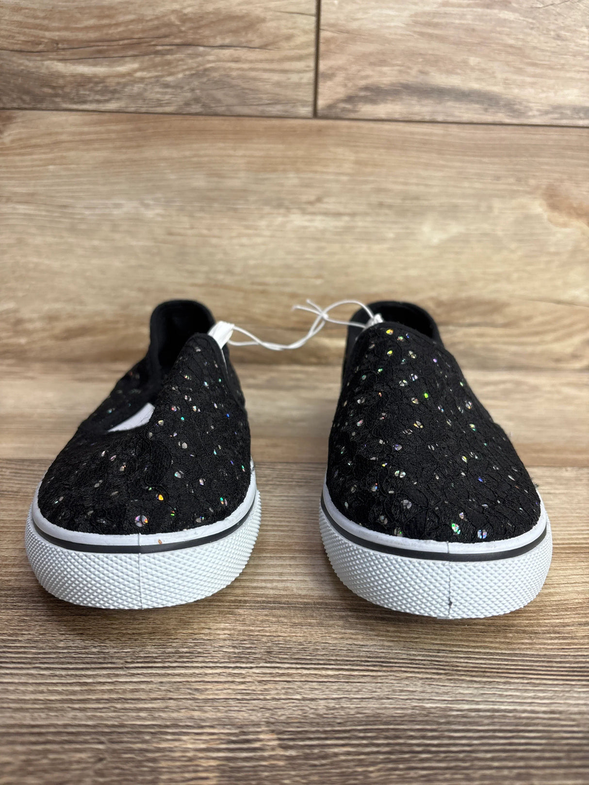 Pair of black kids slip-on sneakers with white soles and glitter accents on wooden floor