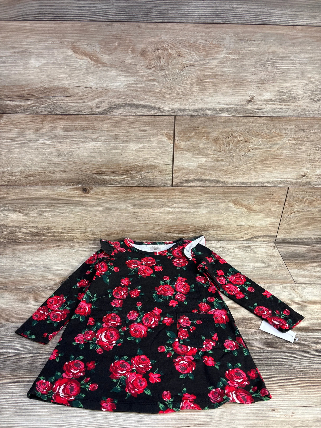 Black long-sleeve toddler dress with red rose floral print and front pocket on wood floor