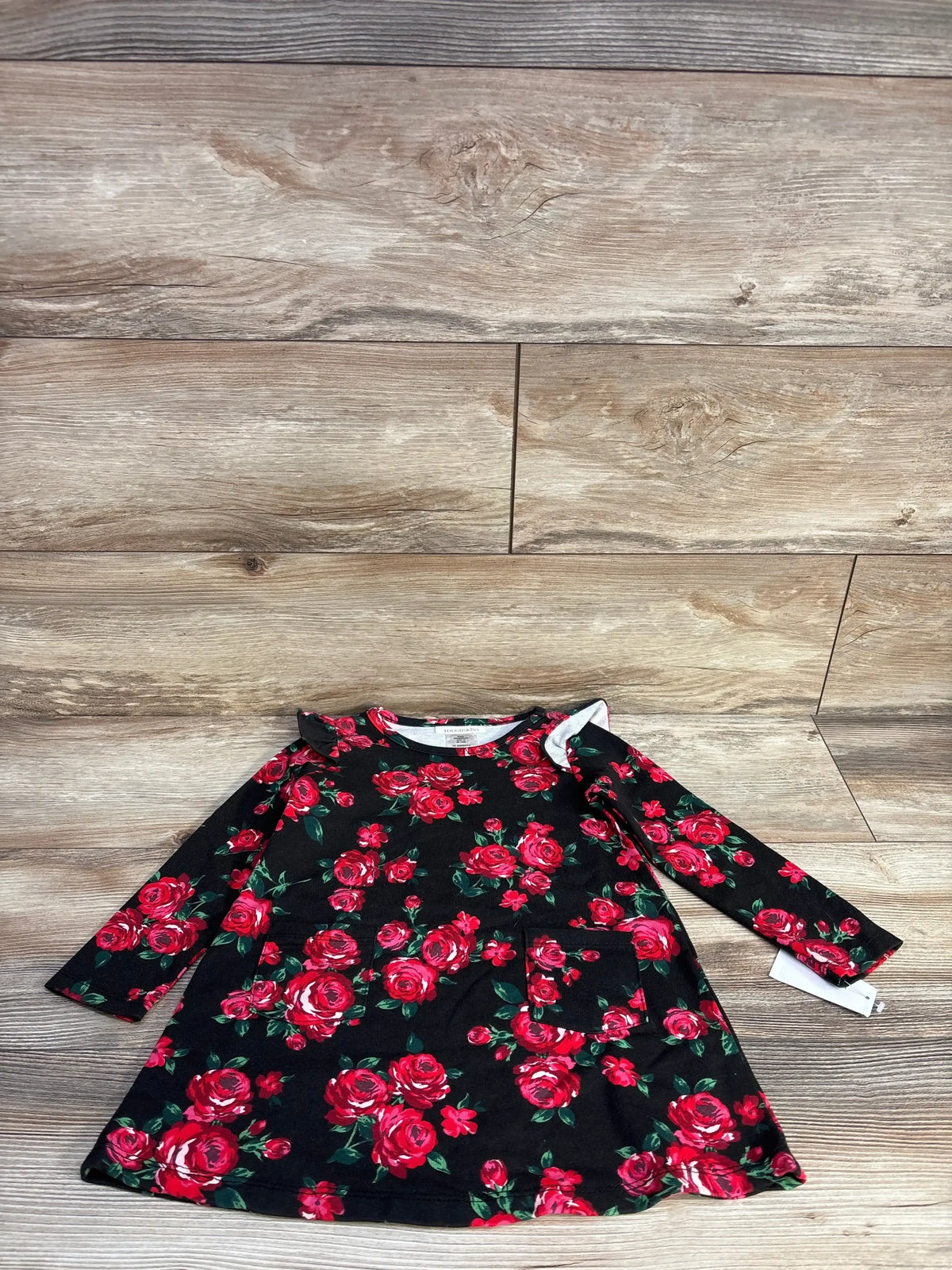 Black long-sleeve toddler dress with red rose floral print and front pocket on wood floor