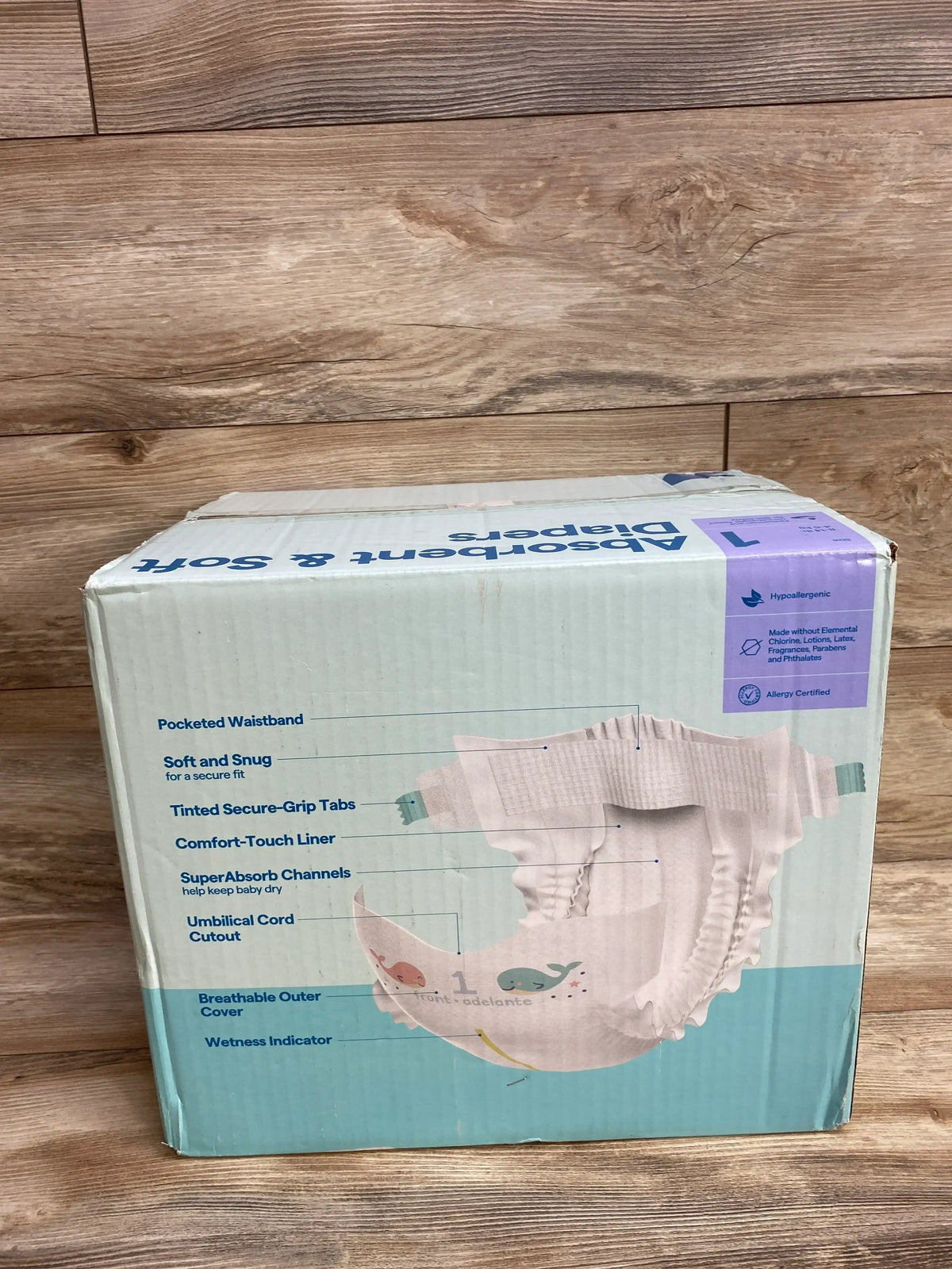 Box of hypoallergenic large baby diapers with features list and whale design on wood floor