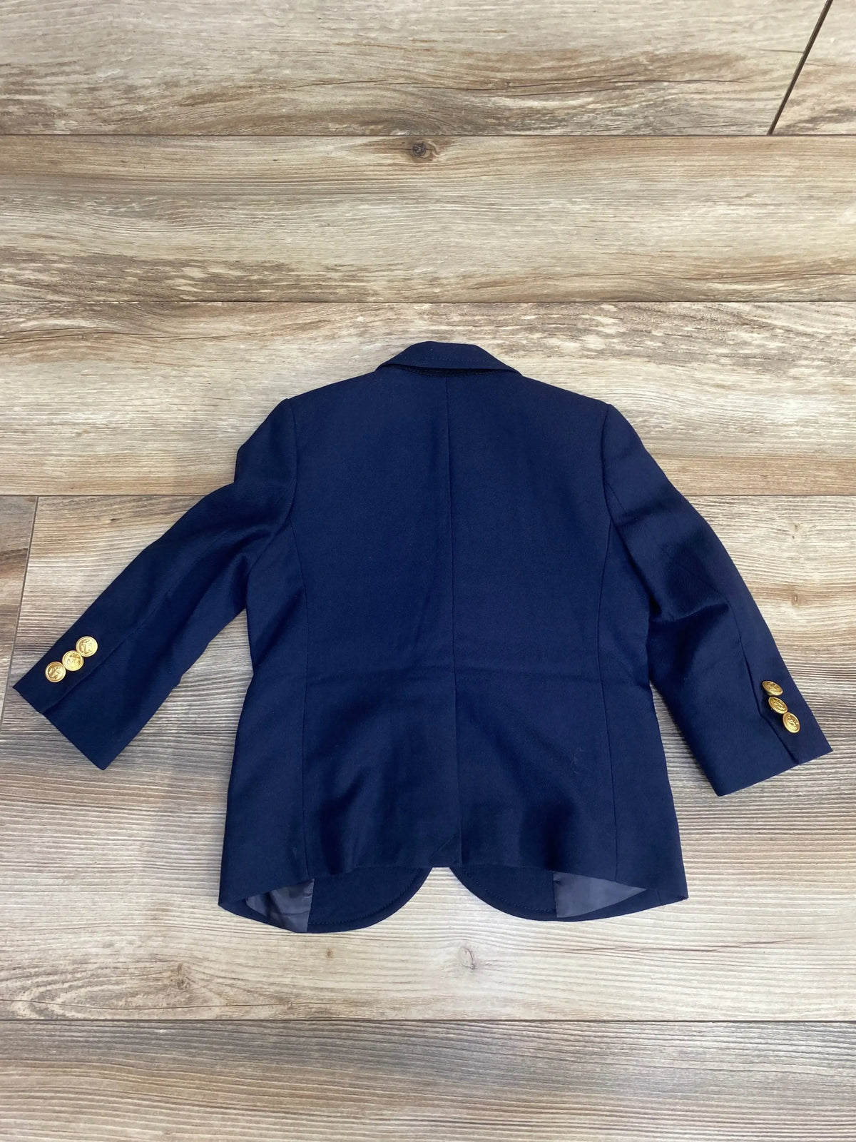 Back view of Crewcuts navy toddler blazer (size 2T) showing gold sleeve buttons and scalloped back hem on wood floor