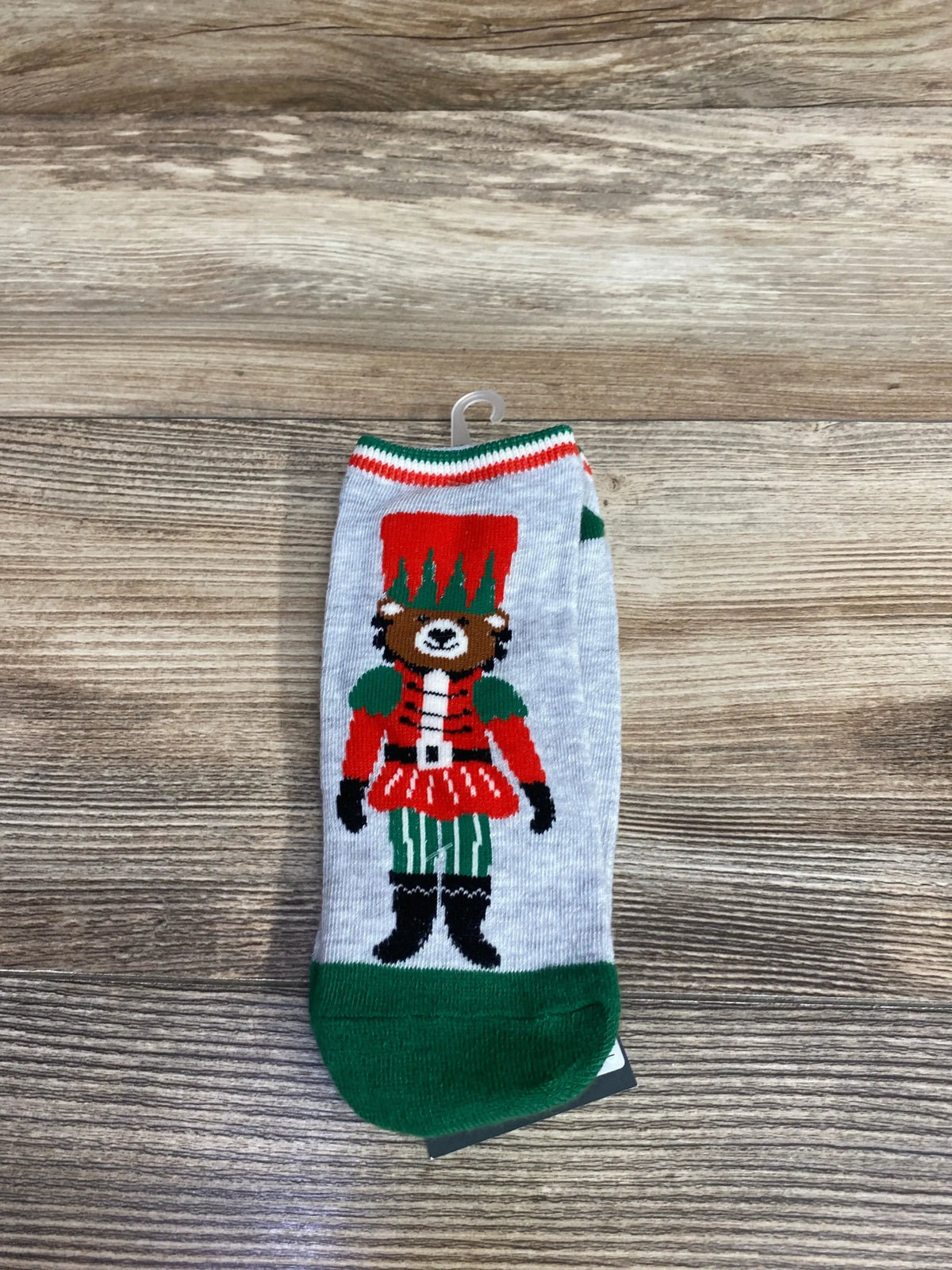 Gray sock with green toe featuring a colorful bear dressed as a nutcracker soldier on a wooden surface